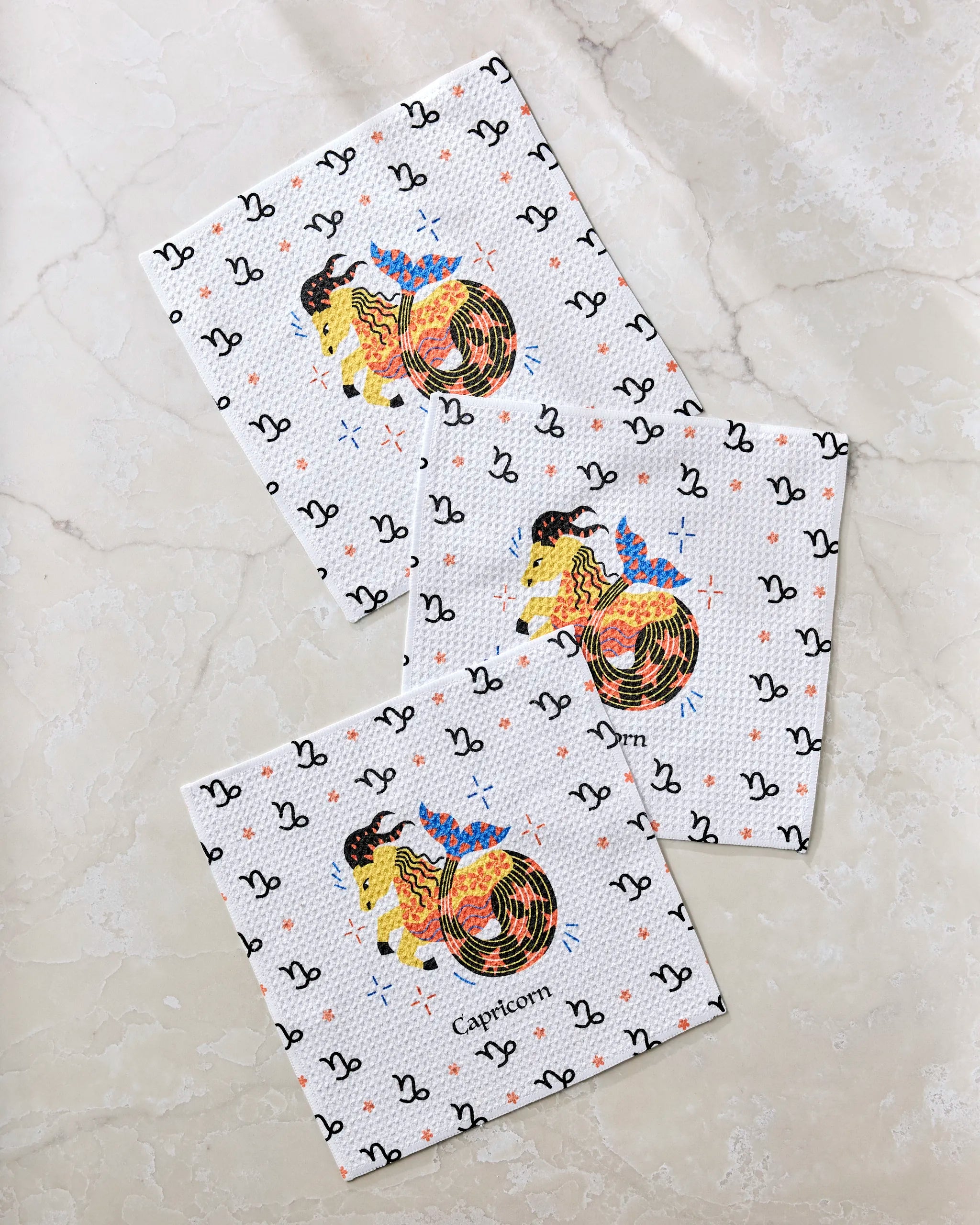Three white recycled dishcloths from Heather Zhou, featuring the Steadfast Capricorn design—a colorful Capricorn goat with black zodiac symbols and "Capricorn" in the center—make an absorbent, stylish kitchen towels set for any space.