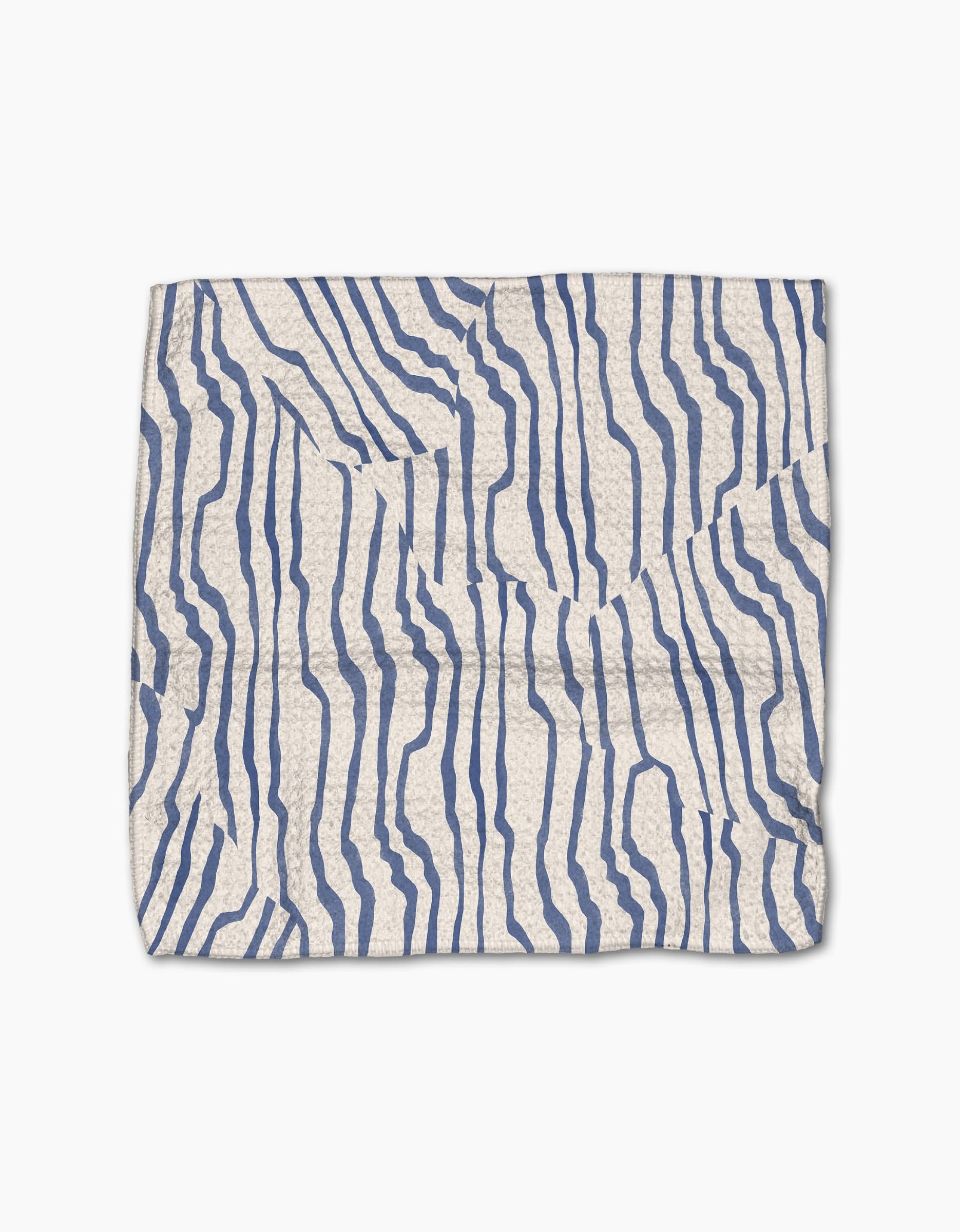 The Geometry Stripe Funk Grounds is a rectangular white dishcloth made from Geoweave fabric, featuring an abstract pattern of irregular wavy blue lines and visible creases on its surface.