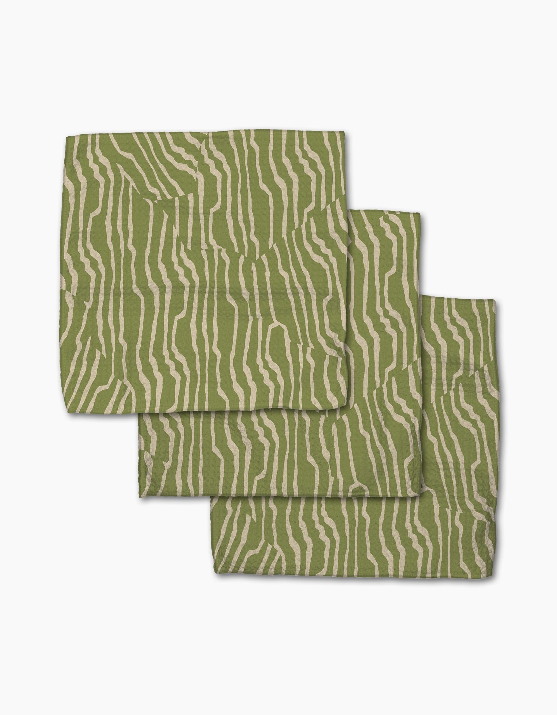 Three Stripe Funk Grounds Green placemats by Geometry, made from recycled materials, display wavy beige zebra-like stripes on green and are stacked slightly offset on a white background.