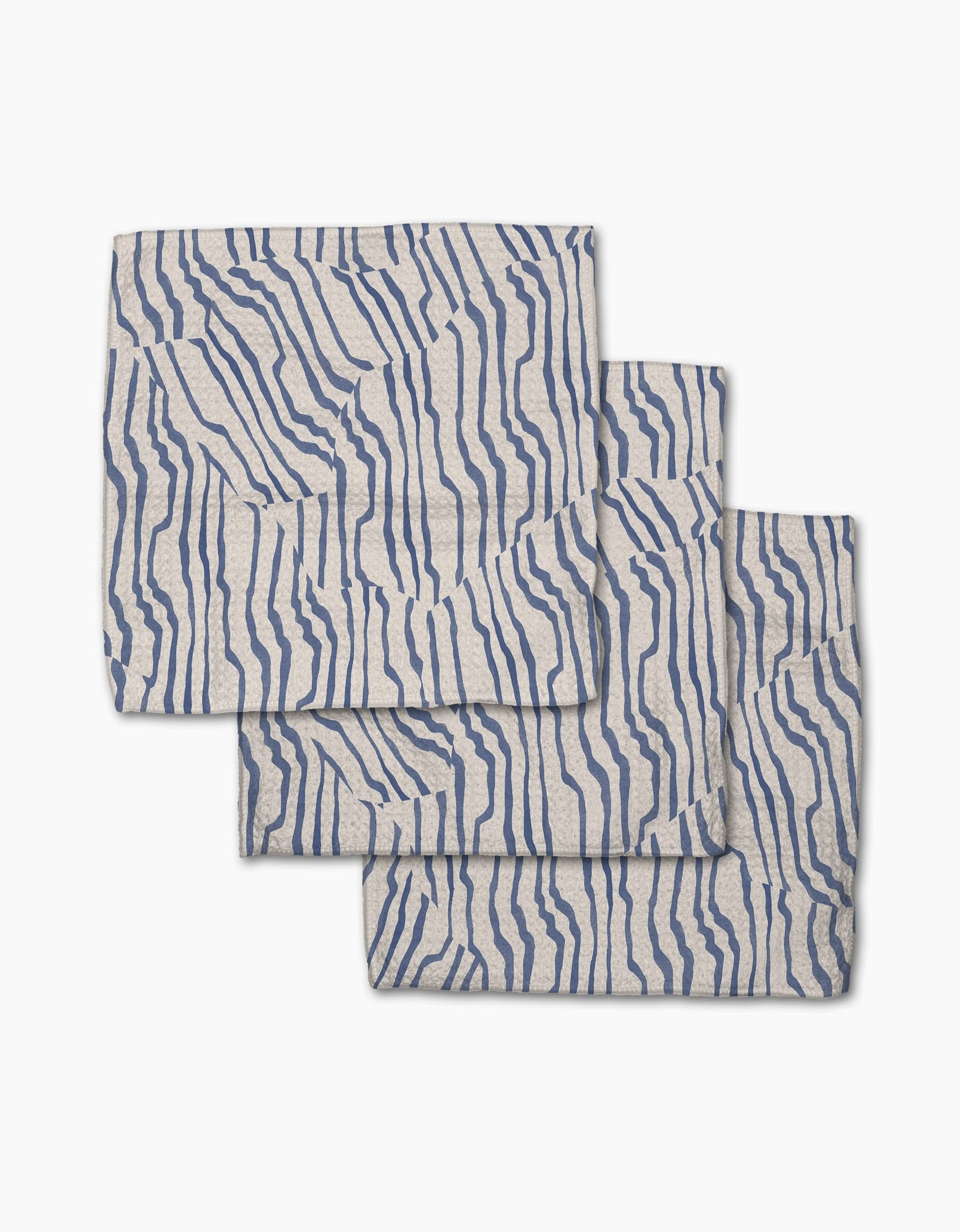 Three folded Stripe Funk Grounds napkins by Geometry, made from recycled materials, feature an abstract wavy blue line pattern and are stacked with slight overlap on a white background.