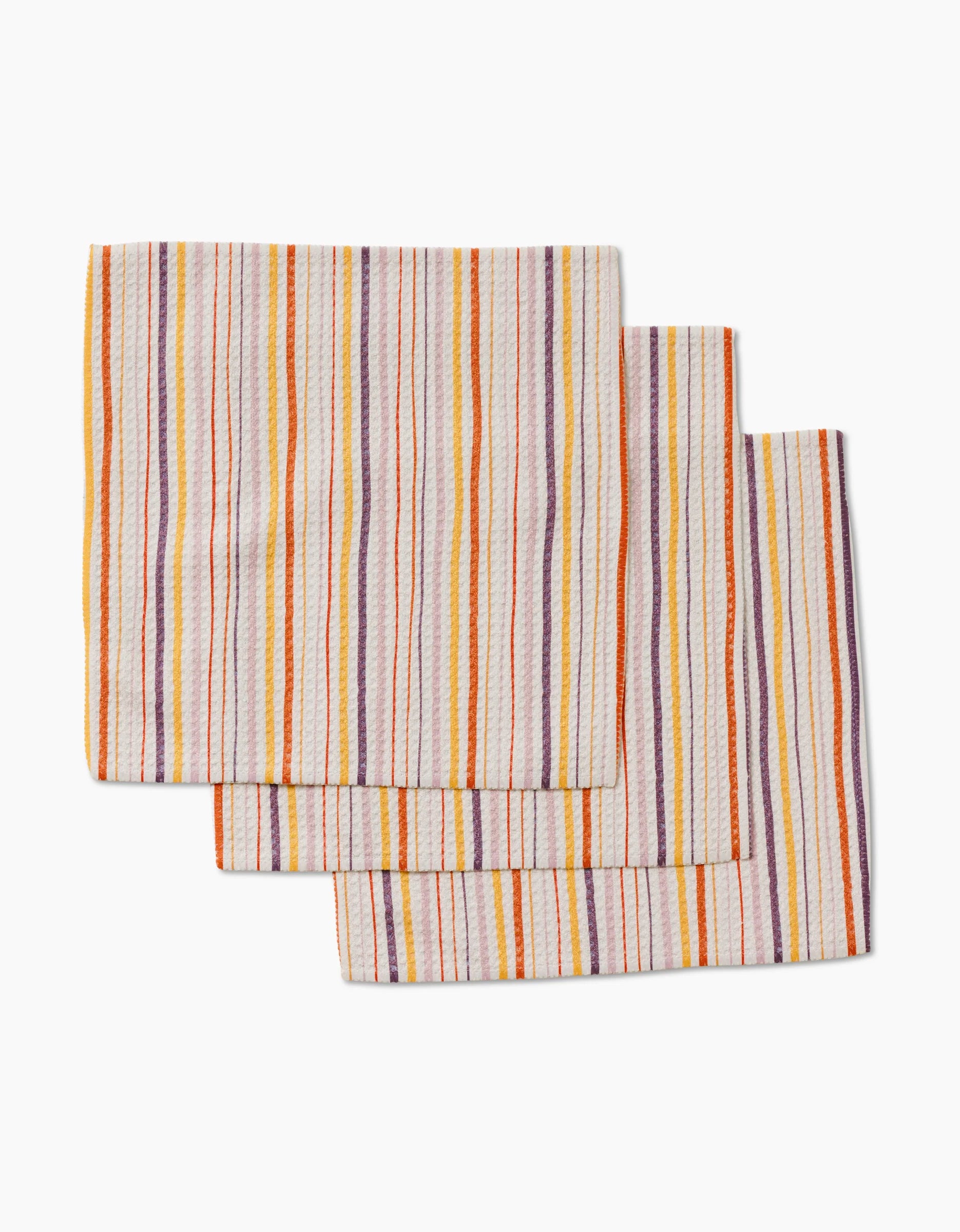 Three Stripe Season dishcloths by GEOMETRY, featuring vertical stripes in orange, yellow, red, and purple on white. Made from super-absorbent recycled materials and stacked with overlapping edges.