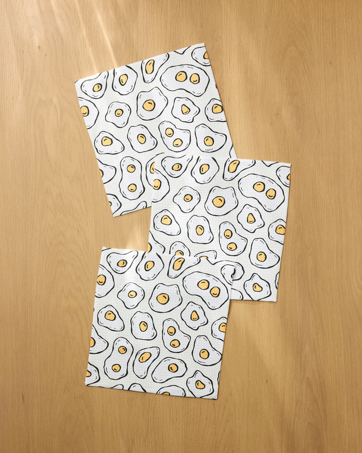 The Rosa Kichline Sunny Side Eggs set includes three eco-friendly, rectangular dishcloths with a playful fried egg cartoon pattern—perfect for adding fun and function to your kitchen.