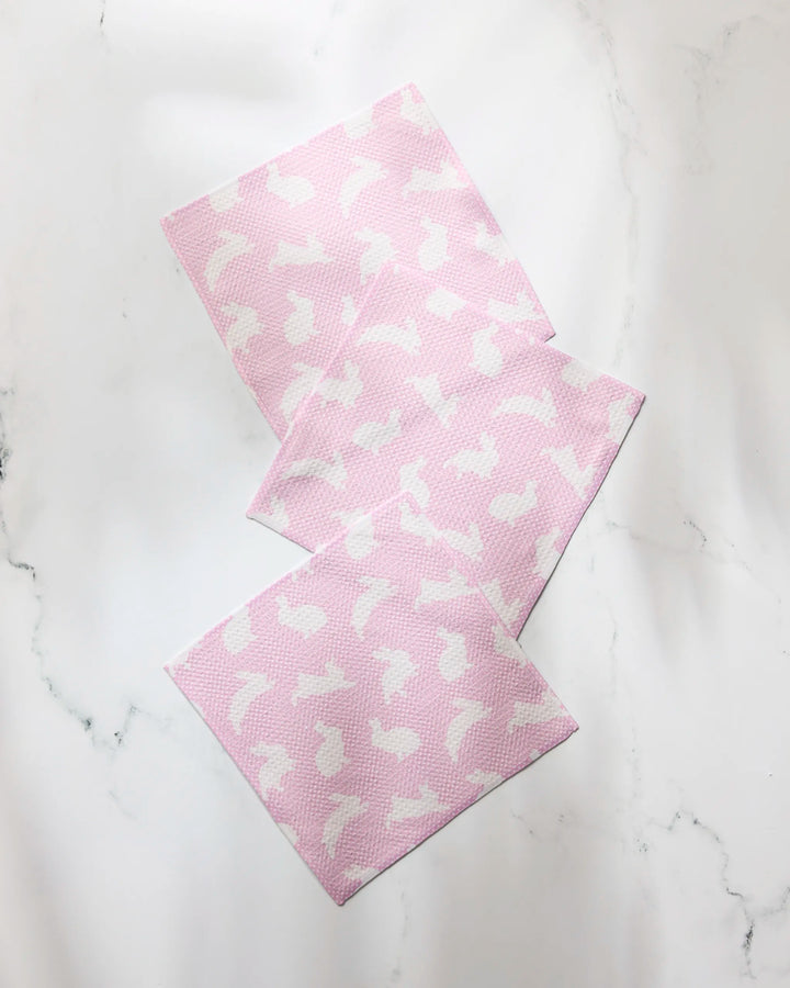 Three Geometry Sweet Bunny pink super-absorbent dishtowels, featuring a white bunny pattern, are arranged overlapping on a white marble surface.