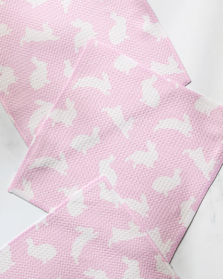 Four textured light pink napkins from Geometry’s Sweet Bunny collection, each with white bunny silhouettes, are arranged overlapping on a white marble background—a charming set made from recycled materials.