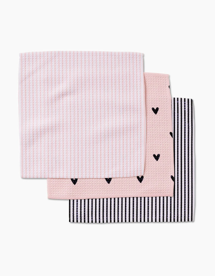 Three folded Sweet Hearts baby washcloths by Kailee Wright are stacked: the top is pink with white stripes, the middle is pink with small black hearts, and the bottom has black and white stripes. Made from Geoweave fabric.
