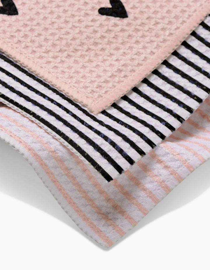 Close-up of Kailee Wrights Sweet Hearts dishcloths: one pink with black hearts, one white with black stripes, and one white with pink stripes—each made from recycled materials.