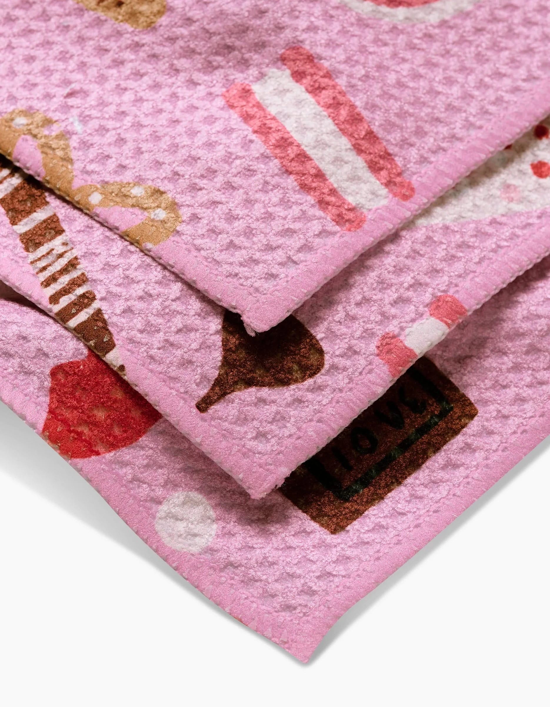 A close-up of Janna Sue Designs Sweet Lovin Geoweave fabric shows a pink waffle texture with colorful prints of candies, pretzels, and a love chocolate. Neatly folded, its perfect for dishcloths.