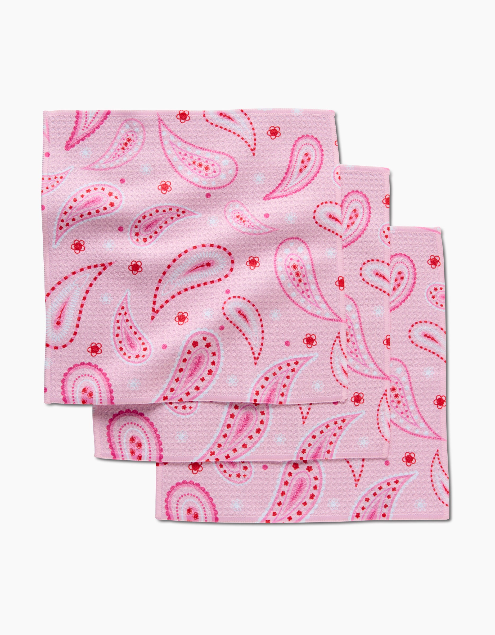 Three Sweet Paisley napkins by GEOMETRY, crafted from recycled materials, feature a paisley pattern in pink and red hues and are arranged in an overlapping stack on a white background.