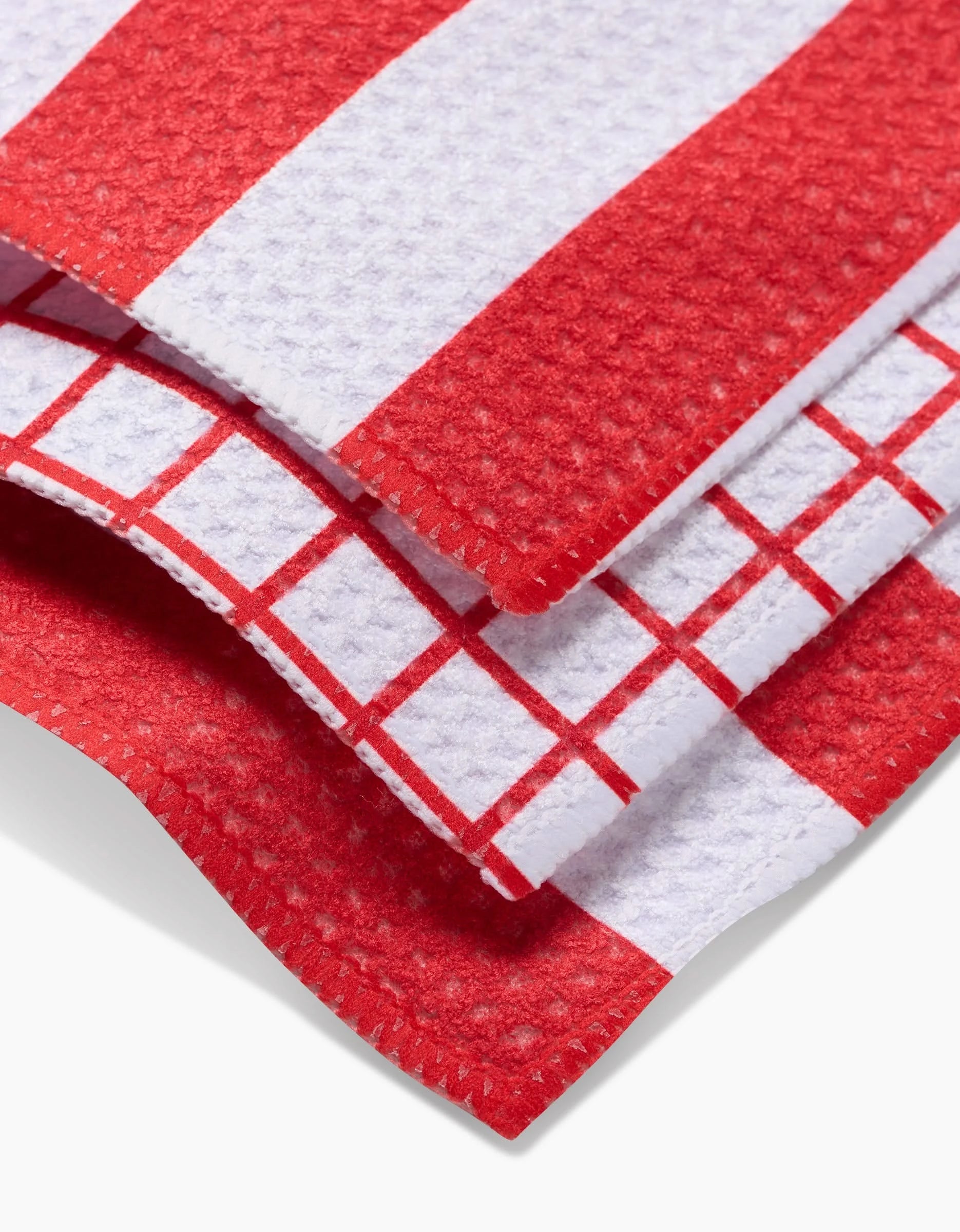 Close-up of Kailee Wright’s Sweet Peppermint Dishcloth Set: three folded towels with red and white patterns—wide stripes, thin stripes, and grid—all with a textured, waffle-like surface for fast drying.
