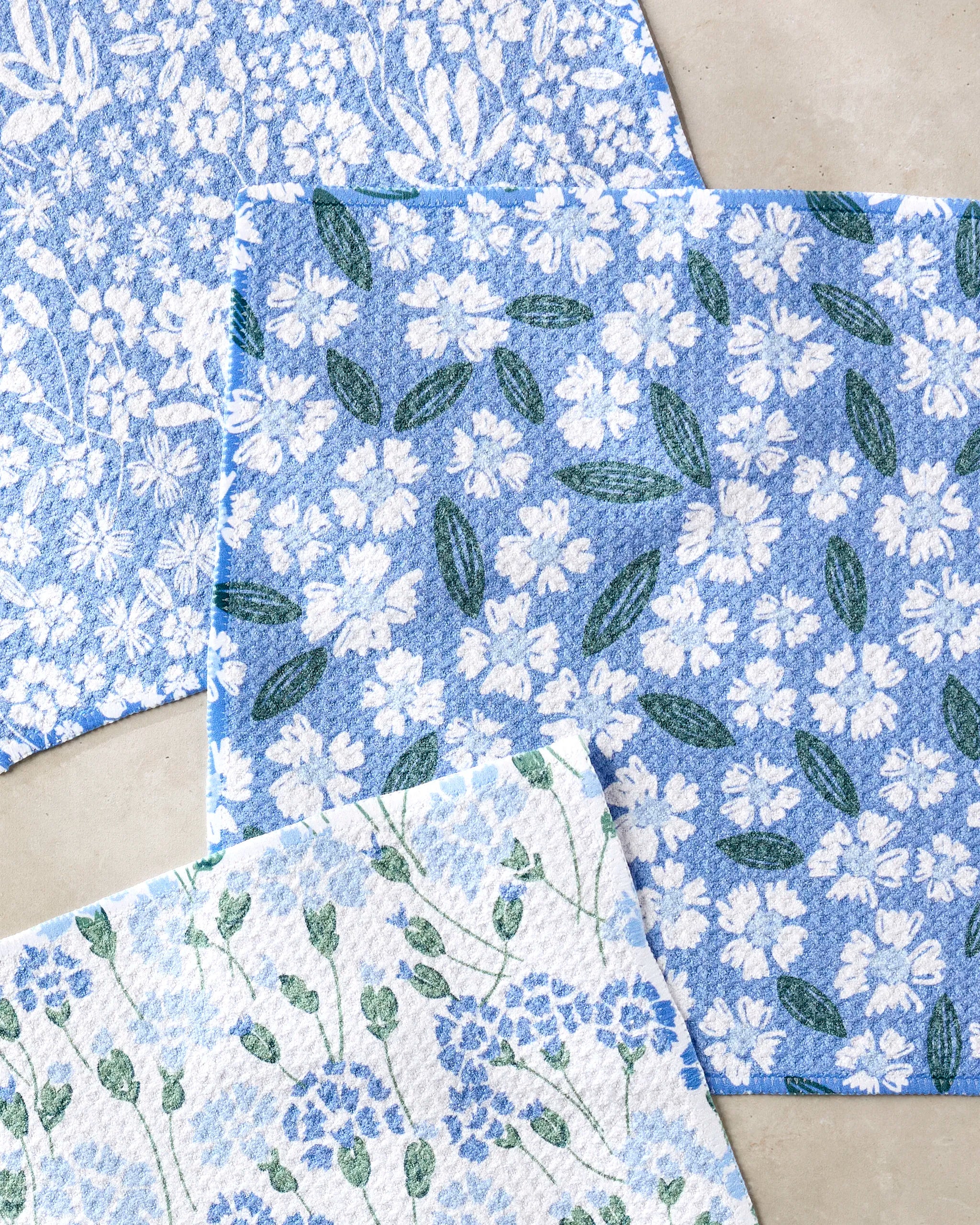 The Sweetie Floral dishcloth set by Hufton Studio features blue and white colors with white flowers, made from recycled materials for an eco-friendly touch.