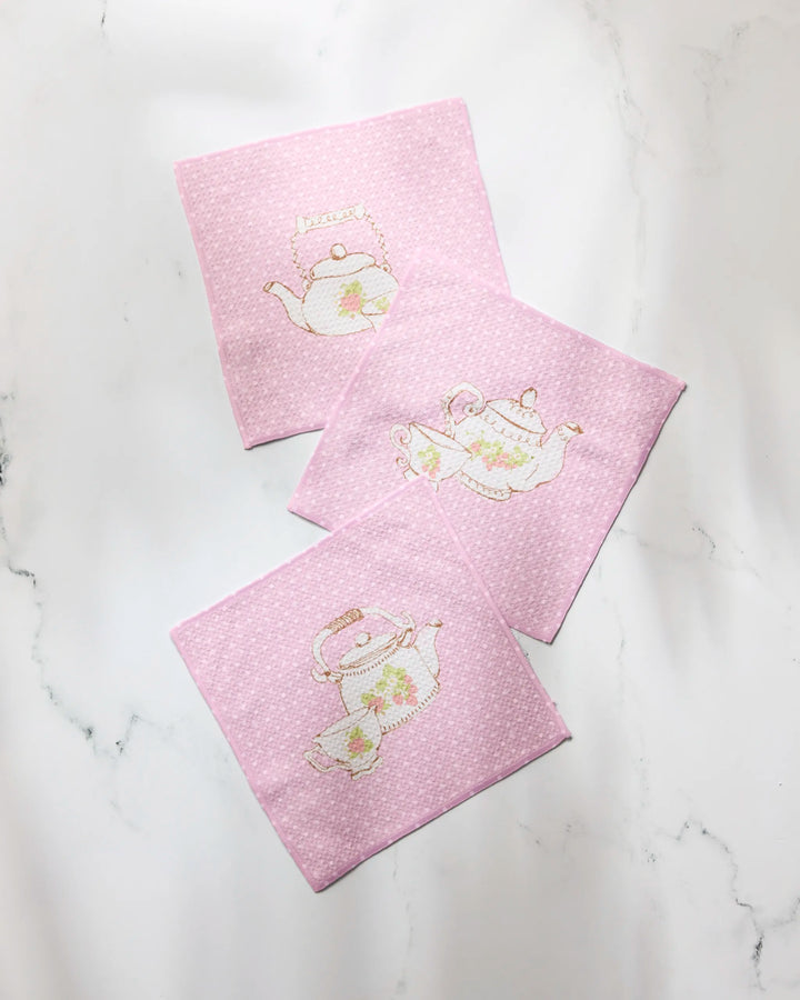 Three "Tea Time" coasters by Geometry, made from recycled pink dish towels with light polka dots and teapot embroidery, are displayed on a white marble surface.
