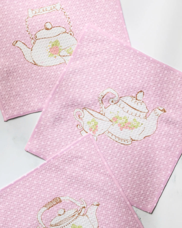 Geometry's Tea Time set features four light pink napkins with a subtle textured pattern and vintage floral teapot illustrations, adding a charming touch to your dishcloth collection and enhancing any table setting.