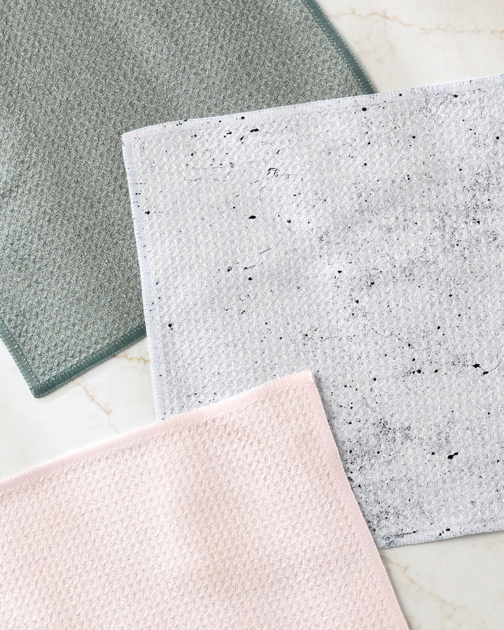 Three rectangular cloths from The Wright Set by Kailee Wright are laid out in green, light pink, and white with black speckles. Each towel features a subtle waffle pattern for added absorbency.