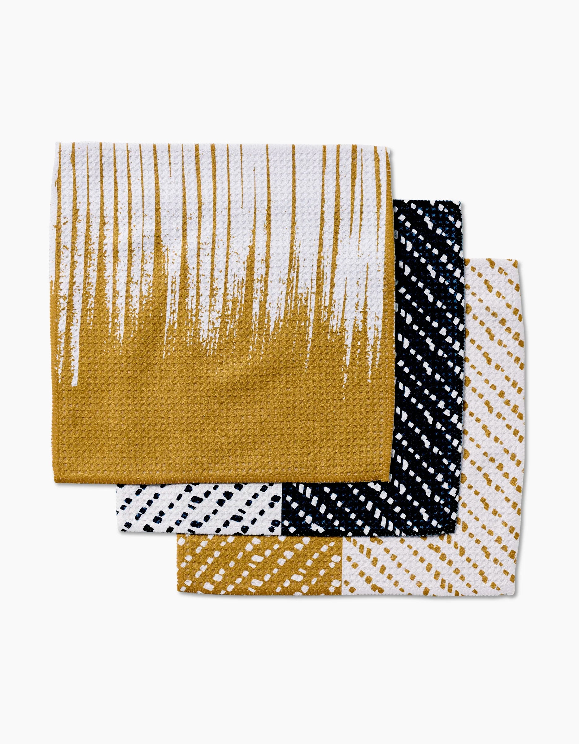 The GEOMETRY This And That set includes three folded textured dish towels made from recycled materials with modern patterns in mustard yellow, black, and white.