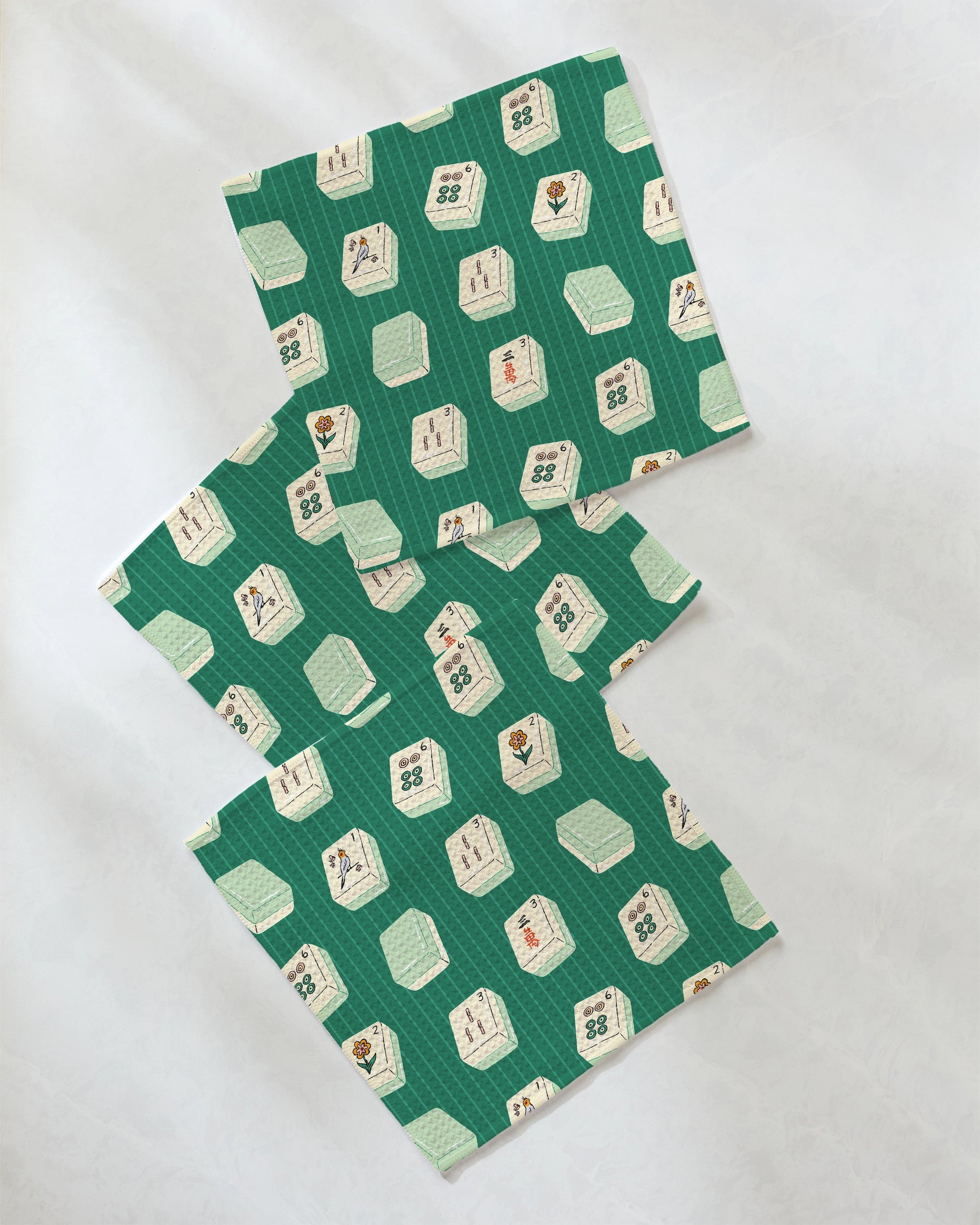 Three green fabric squares with a repeating mahjong tile pattern are arranged in a zigzag shape on a white background, highlighting the Tile Flow dishcloth set by Geometry. These eco-friendly dishcloths are thoughtfully designed to add both playful style and practicality to any kitchen.