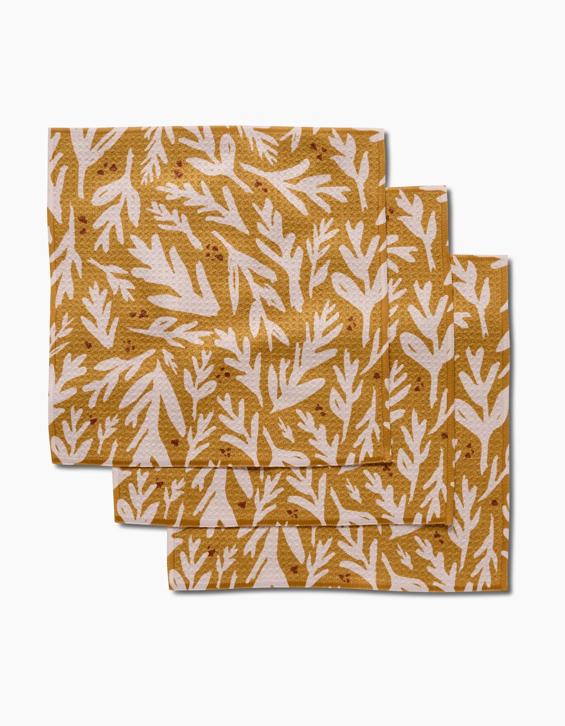 Three Trail Dusting Gold cloths by Twig + Spark, featuring white botanical leaf patterns on mustard yellow and made from recycled materials, are stacked with slight overlap on a white background.