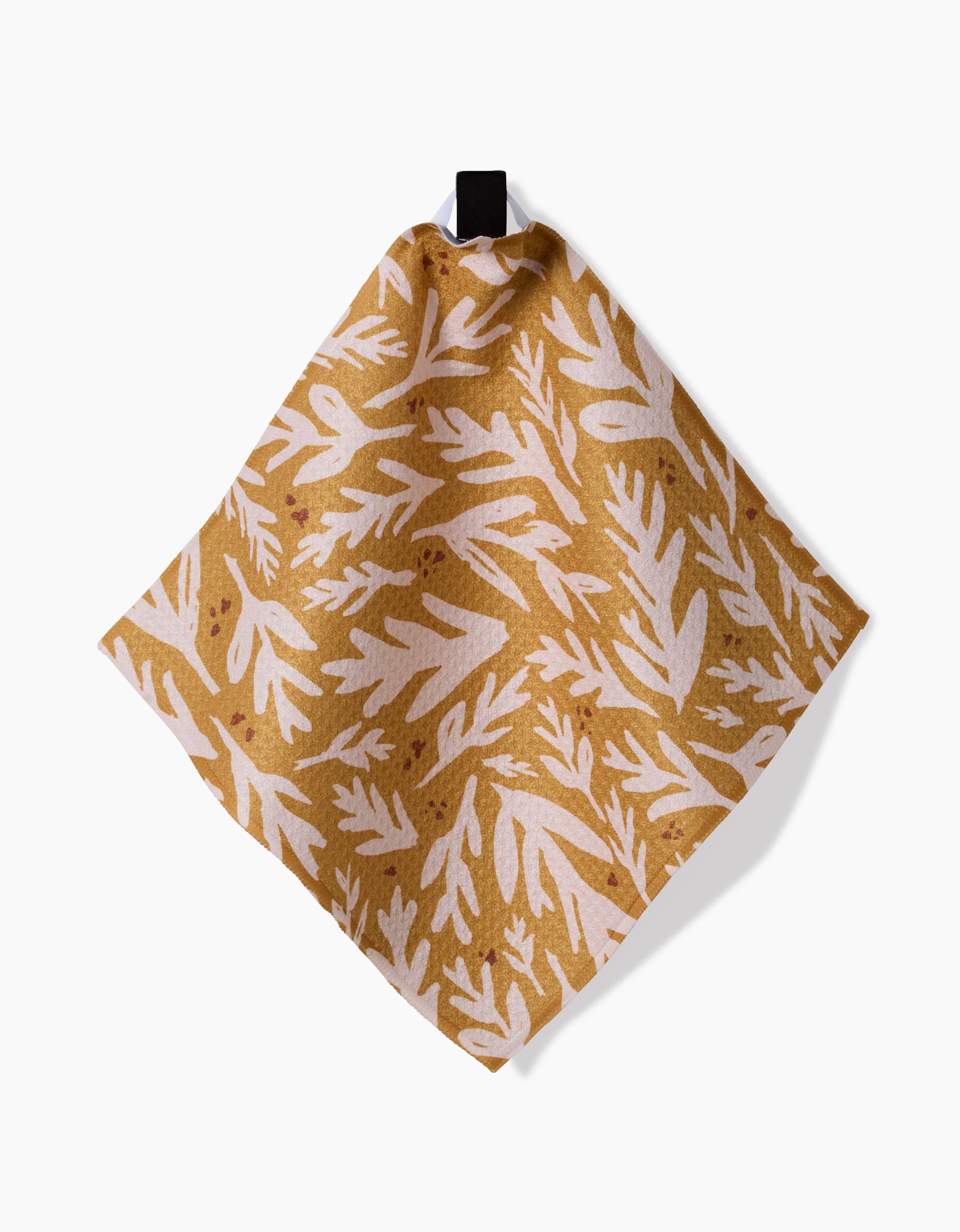 Trail Dusting Gold by Twig + Spark is a square tan cloth with a white botanical leaf pattern, made from recycled materials and hanging from a black loop against a white background.