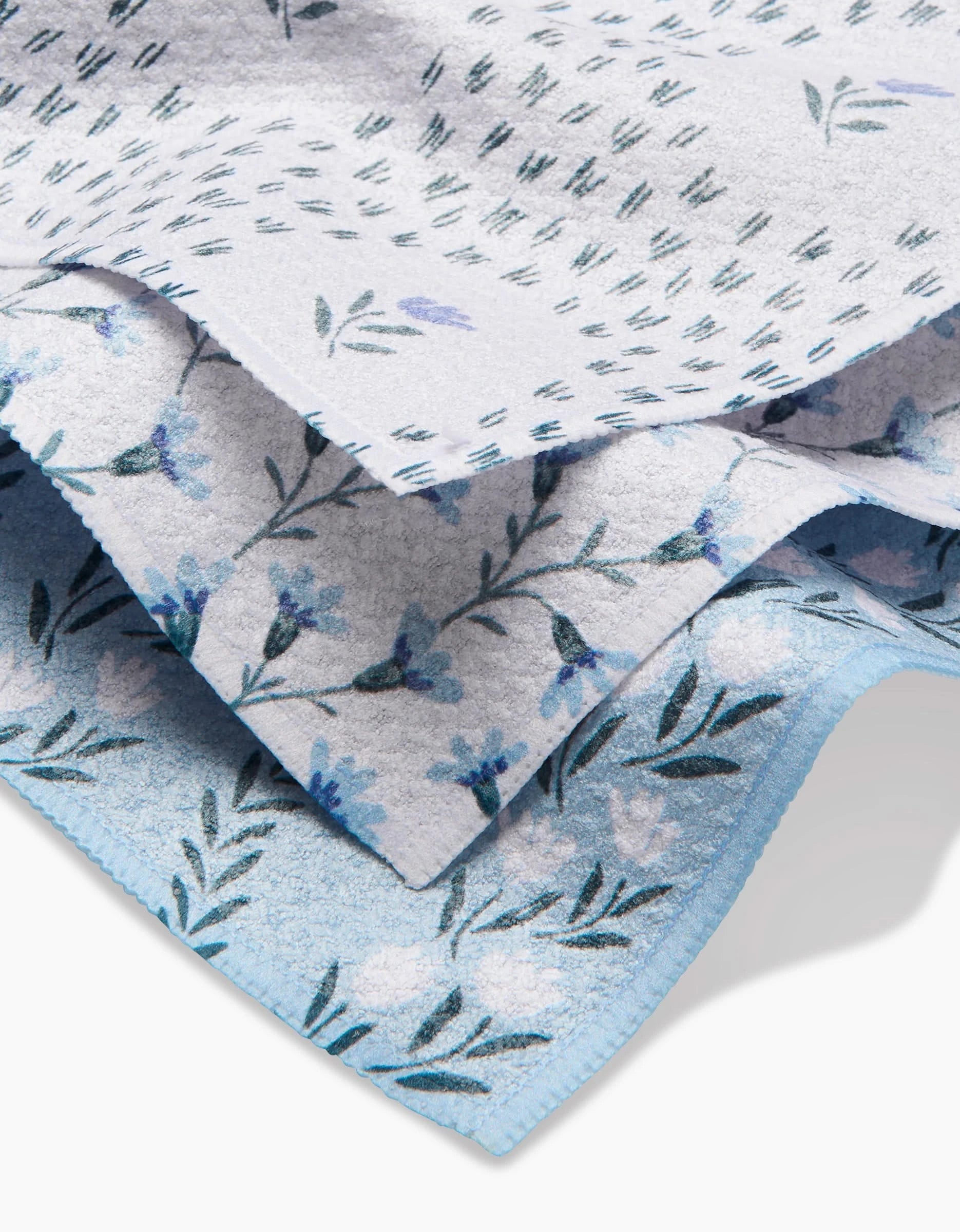 Three stacked Trailing Farmhouse Florals by Teri the Butter, featuring blue floral and leaf patterns in shades of blue, white, and green on a light Geoweave fabric—soft, plush, and perfect for dishcloths. Slightly textured edges add detail.