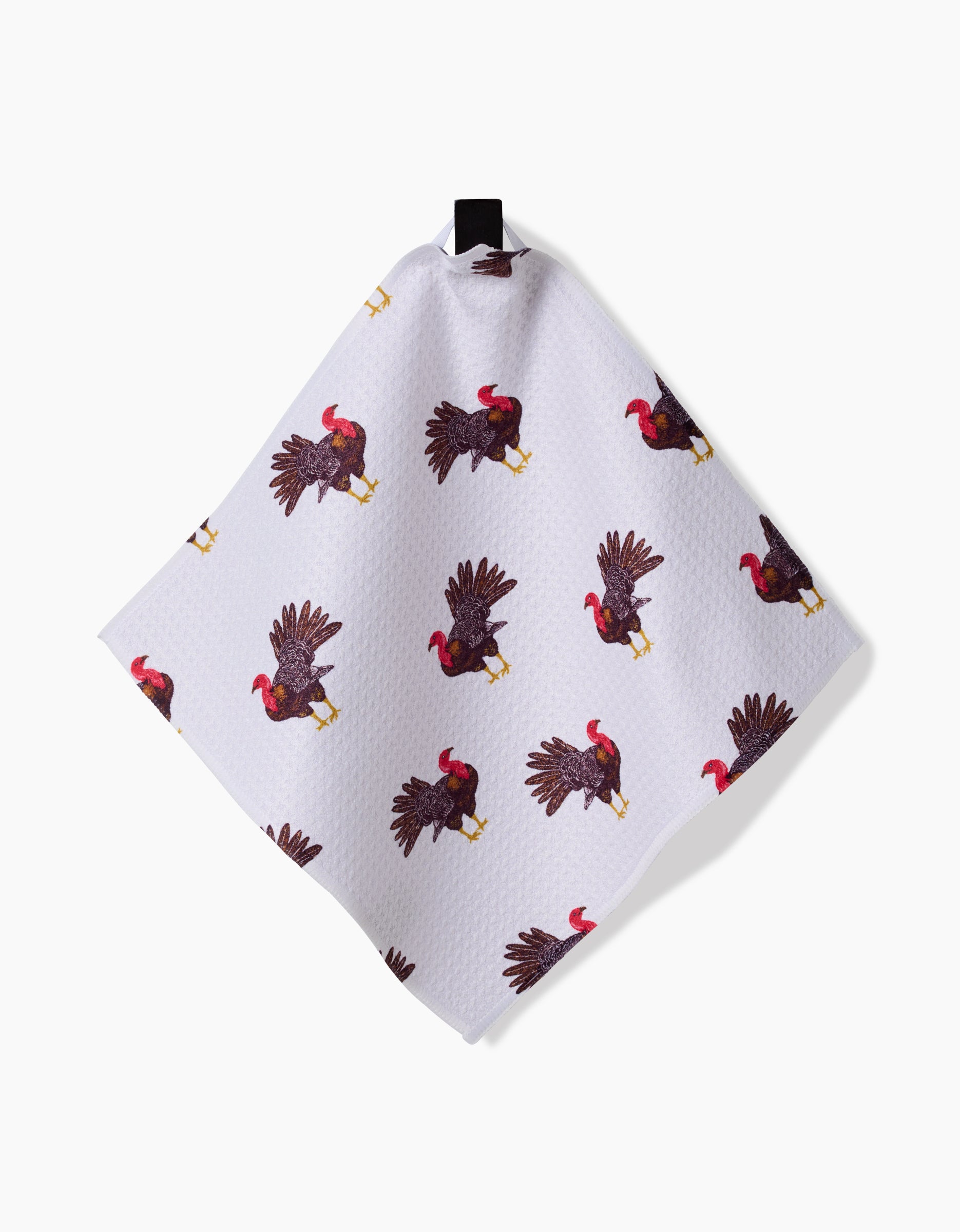 The Turkey Day Parade towel by Vaishali Design Studio is a white recycled cloth with a pattern of illustrated turkeys in various poses, hanging by a black loop against a white background.