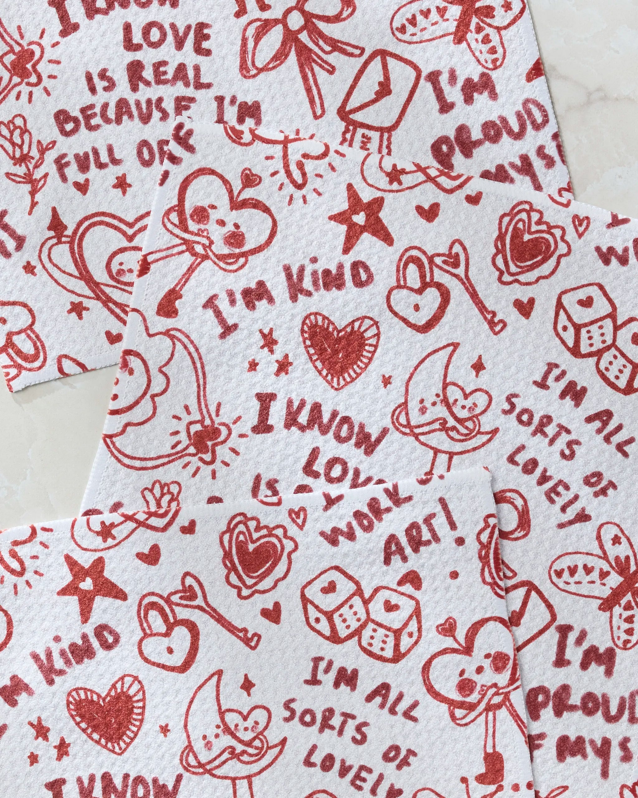 Valentine's Affirmations by Geometry: three recycled paper napkins with red hearts, stars, smiling faces, whimsical drawings, and positive phrases like “I’m kind,” “I know love is work,” and “I’m proud.”.