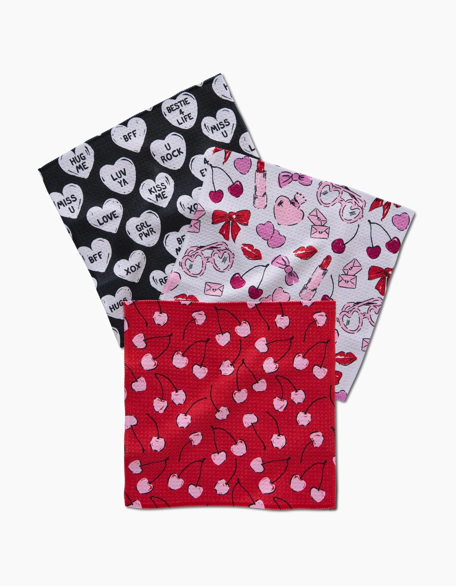 Three eco-friendly Valentines cloth napkins by Hufton Studio, made from recycled materials, feature black, white, and red heart, lip, and cherry patterns overlapping on a white background.