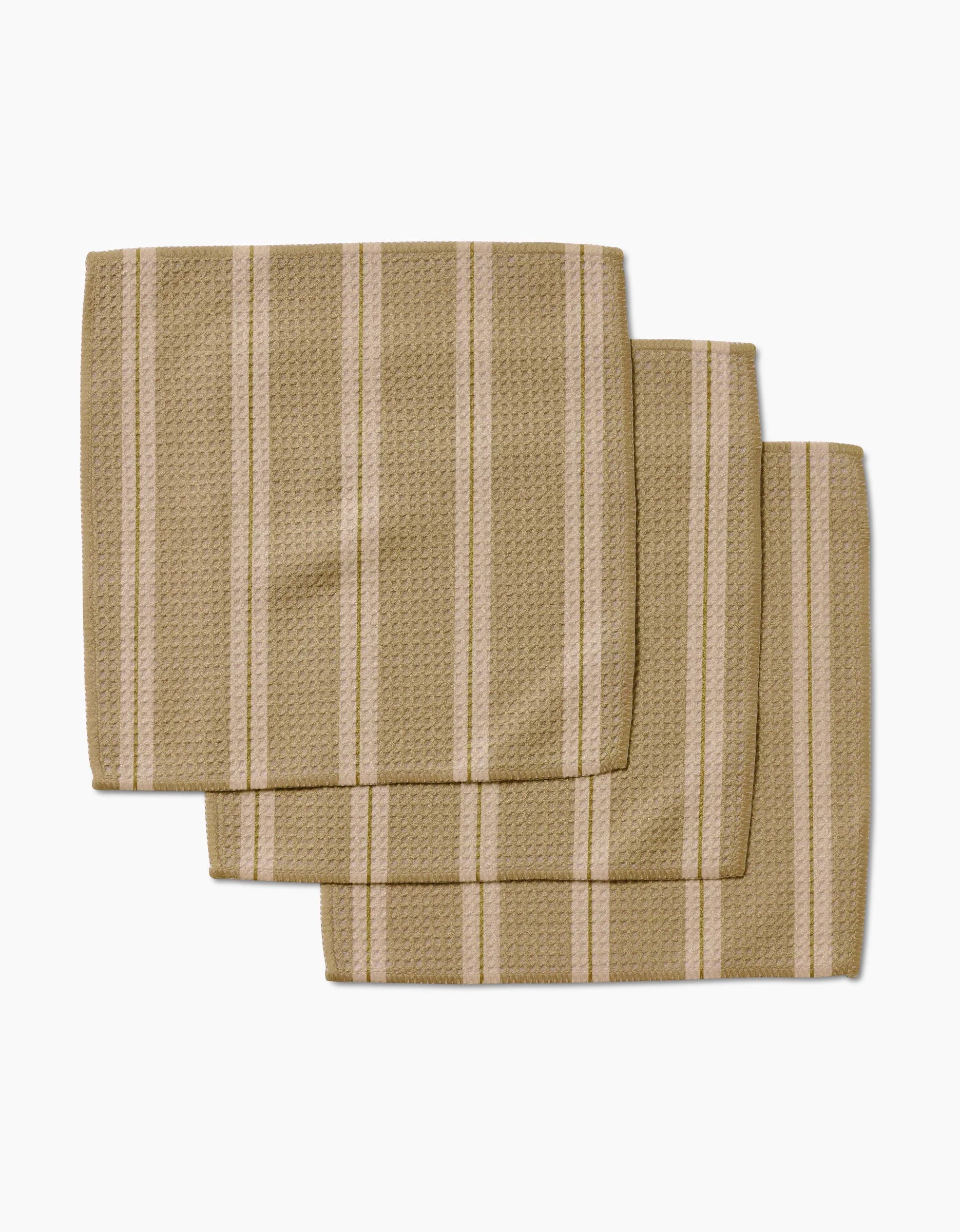 Three overlapping GEOMETRY Vanilla Chai napkins, crafted from Geoweave fabric with a textured surface and vertical white and light brown stripes, are arranged on a white background.
