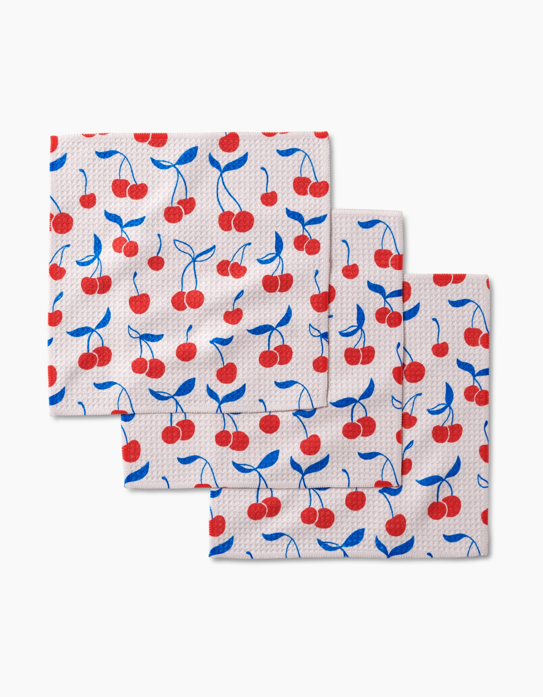 Kayla Anns Very Cherry dishcloths feature a white square design with red cherries and blue leaves, stacked offset on a plain background. Made from super-absorbent Geoweave fabric, they bring style and function to your kitchen.