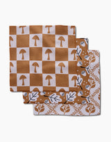 Three folded dishcloths from Charlie Rowan Designs’ Vines Acorns And Mushrooms set are stacked: the top has a tan checkered mushroom pattern, the middle features leafy vines on white, and the bottom shows brown oak leaves—eco-friendly and recycled.