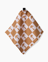 The Vines Acorns And Mushrooms dishcloth by Charlie Rowan Designs features Geoweave fabric with a tan and white checkered pattern, brown mushroom illustrations on the white squares, and hangs from a black loop.