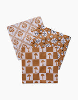 The Vines Acorns And Mushrooms dishcloth set by Charlie Rowan Designs features three overlapping designs—floral diamonds, leaves with acorns, and a checkered mushroom motif—all made from recycled materials in brown and white.