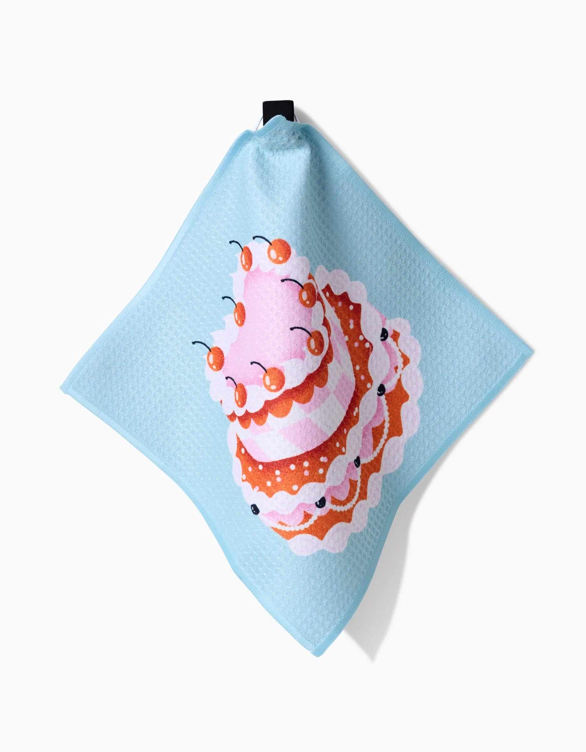 The Megan Roy Vintage Heart Cake is a light blue, super-absorbent cloth featuring a colorful illustration of a pink layer cake with cherries and white frosting, hanging from a black corner loop.