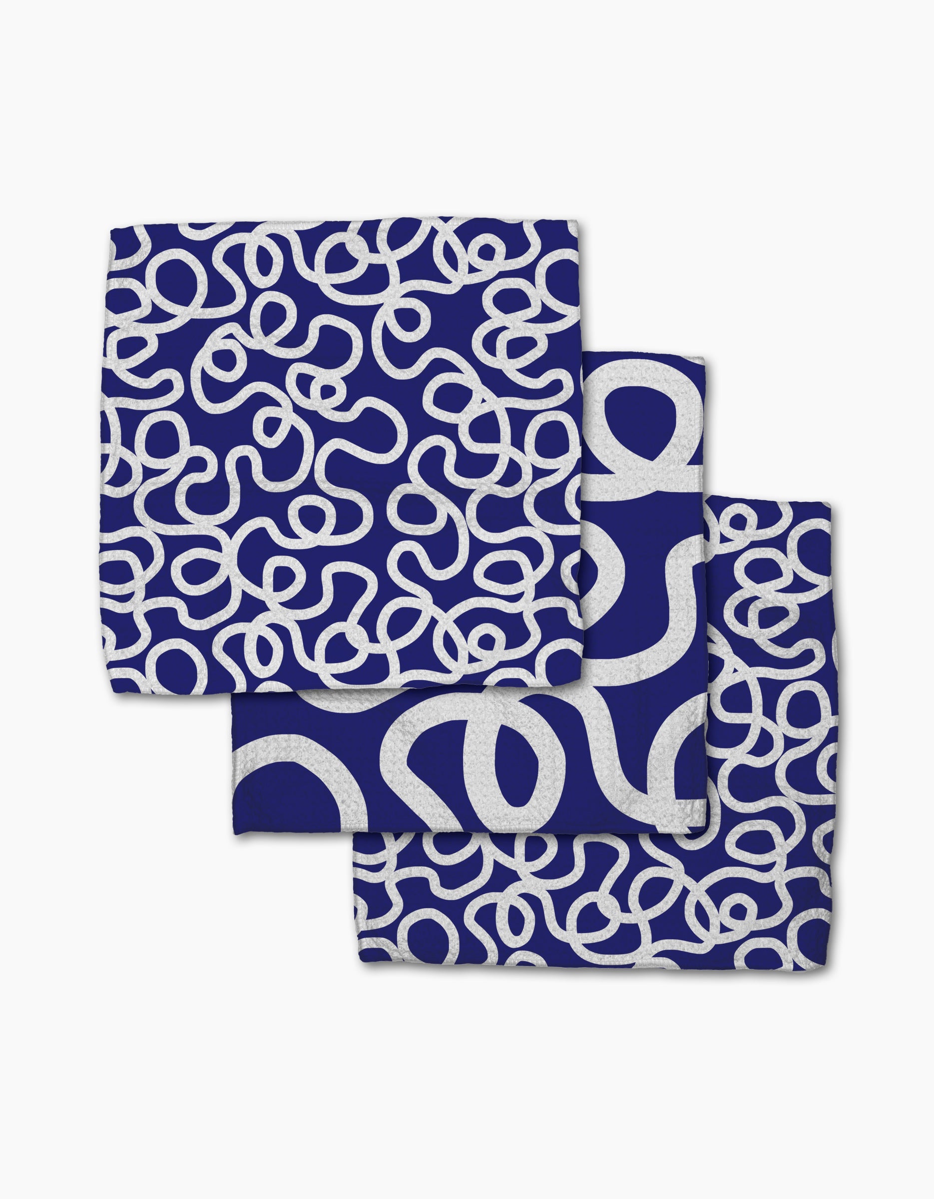 Three folded blue Wander cloth napkins by Rachel Parker, made from recycled materials, display a white abstract looped line pattern with each napkin stacked to show different parts of the design.