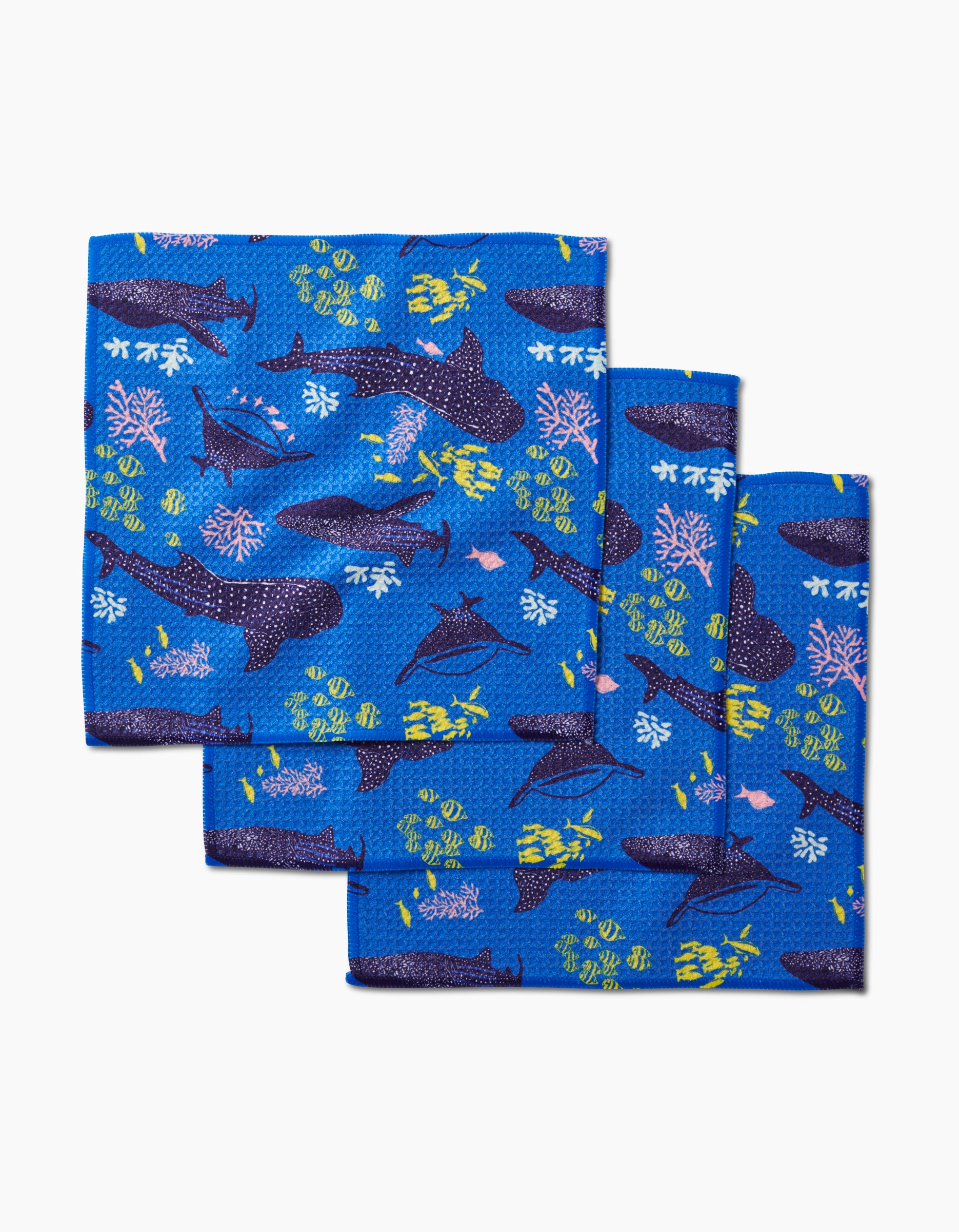 Three folded blue Elisabeth Wing Whale Shark Geoweave dishcloths display a vibrant ocean-themed print with whales, fish, coral, and seaweed in yellow, pink, green, and white on a white background.
