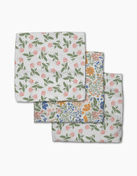 Three folded Wildflower Vine Blush kitchen towels by Danelys Sidron are shown, made from Geoweave fabric—two with a pink and green floral pattern, and one with blue, orange, and pink flowers and green leaves on a white background.