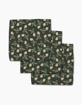 The Danelys Sidron Wildflower Vine Onyx set includes three dark green cloth napkins made from recycled materials, featuring a floral pattern with white and orange flowers and green leaves. The super-absorbent napkins come neatly folded.