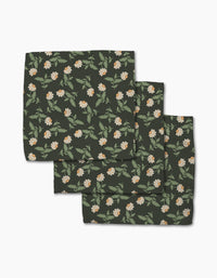 The Danelys Sidron Wildflower Vine Onyx set includes three dark green cloth napkins made from recycled materials, featuring a floral pattern with white and orange flowers and green leaves. The super-absorbent napkins come neatly folded.