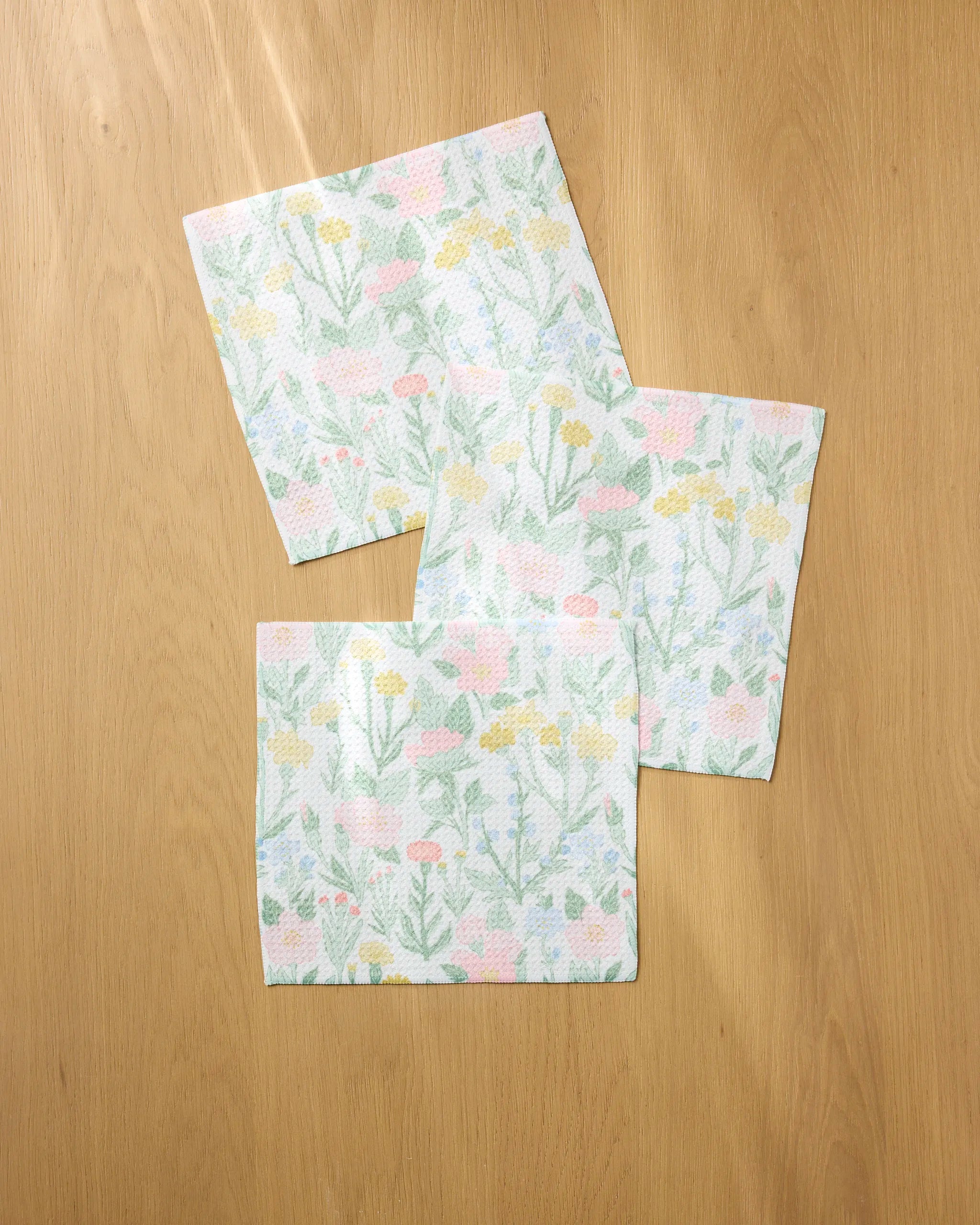 Three "Wildflowers in Bloom" square paper napkins by Jasmine Blooms Designs, made from recycled materials, feature a pastel floral pattern with green stems and yellow and pink flowers—adding an eco-friendly touch to your table setting.