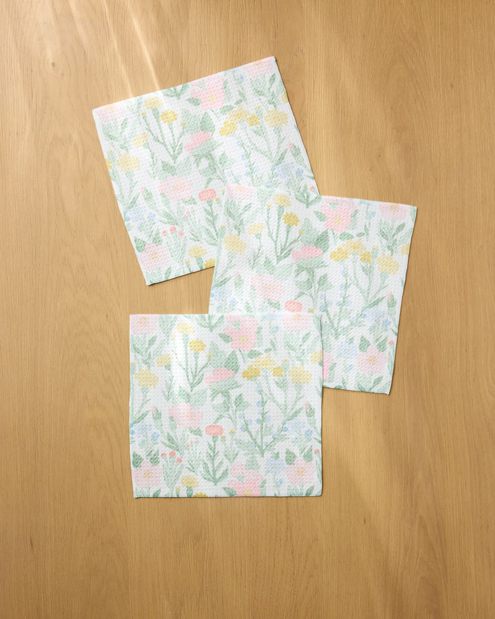 Three "Wildflowers in Bloom" square paper napkins by Jasmine Blooms Designs, made from recycled materials, feature a pastel floral pattern with green stems and yellow and pink flowers—adding an eco-friendly touch to your table setting.