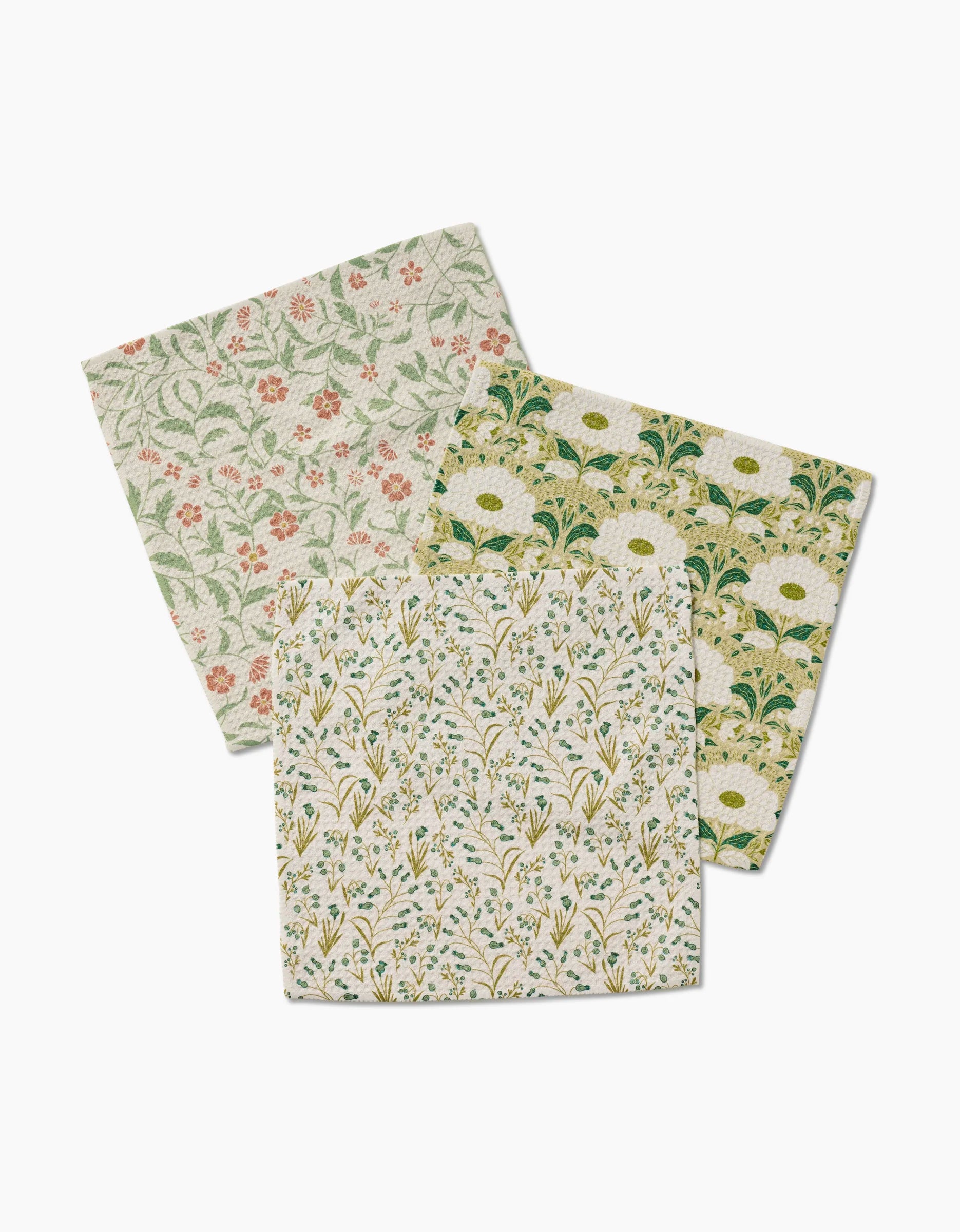 Three square cloth napkins from Danelys Sidron’s Wildlight collection feature Geoweave fabric and floral prints—red and green flowers, yellow with green leaves, and mixed yellow-blue blooms on beige, all artfully overlapped.