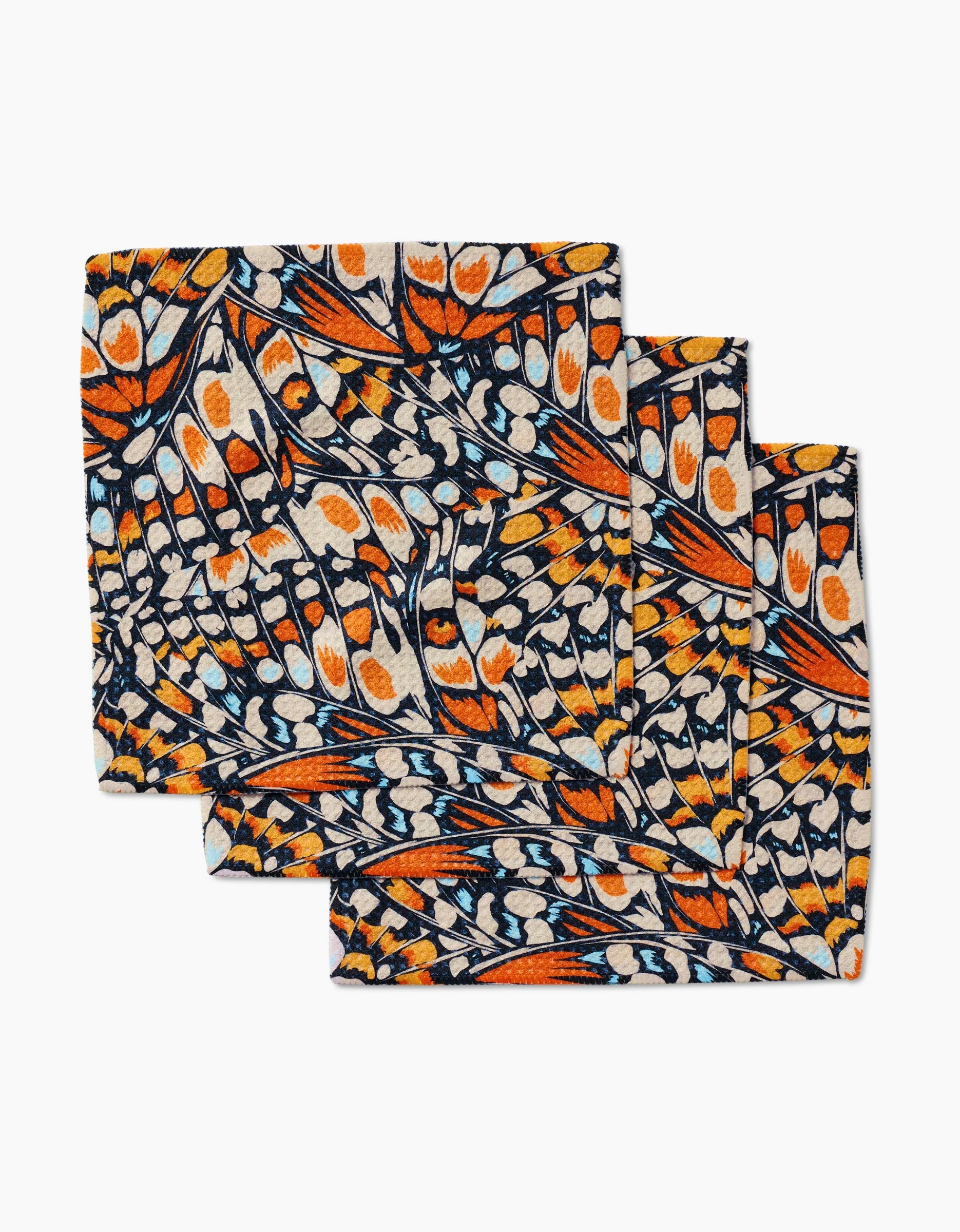 Set of three GEOMETRY Wings in the Wind cloth napkins, crafted from Geoweave fabric and featuring an orange, black, white, and blue butterfly wing pattern with intricate overlapping shapes for a unique look.