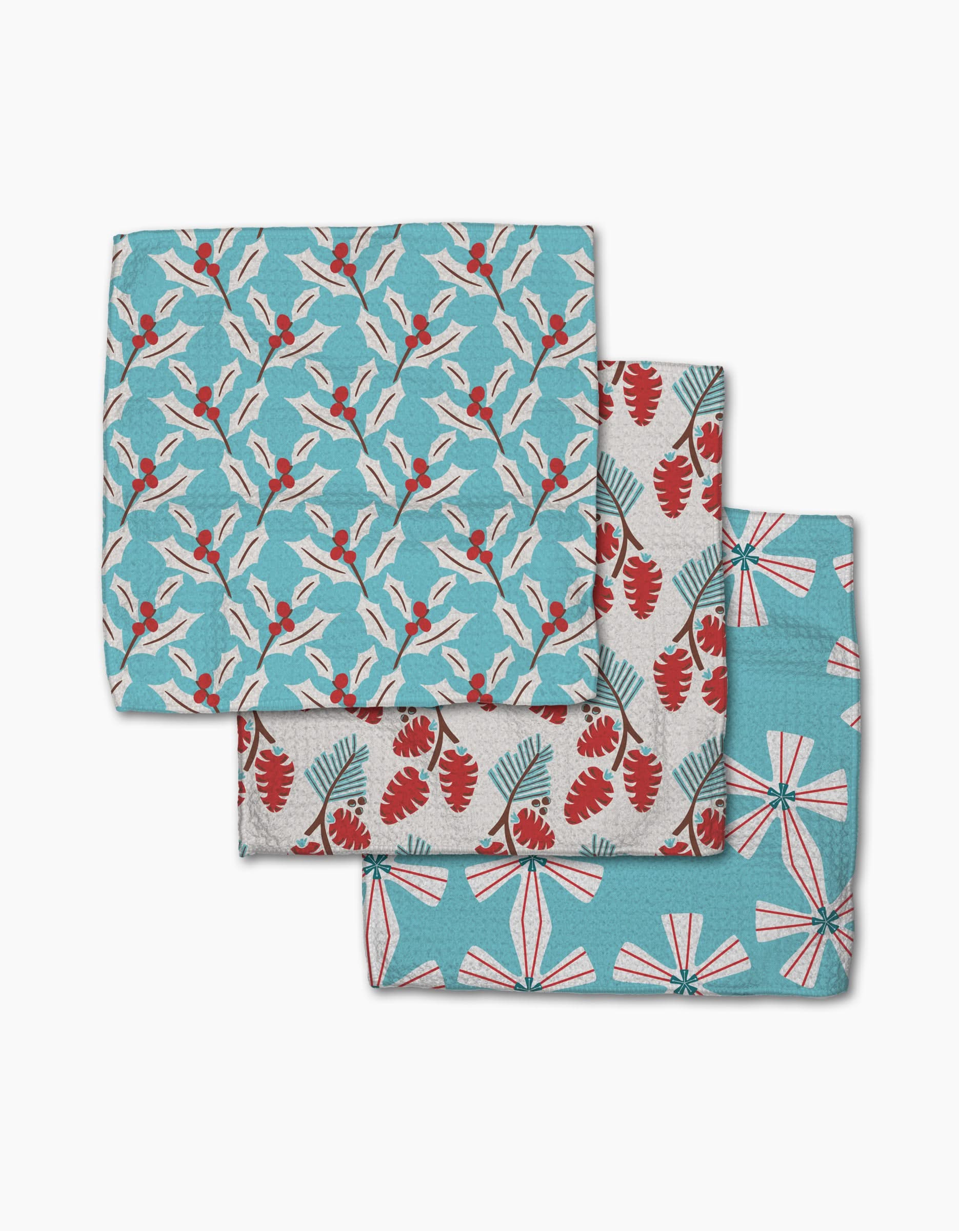 Three folded Winter Holly napkins by Lizzie Clark, made from recycled materials, display blue, red, and white floral and leaf patterns arranged in a staggered stack.