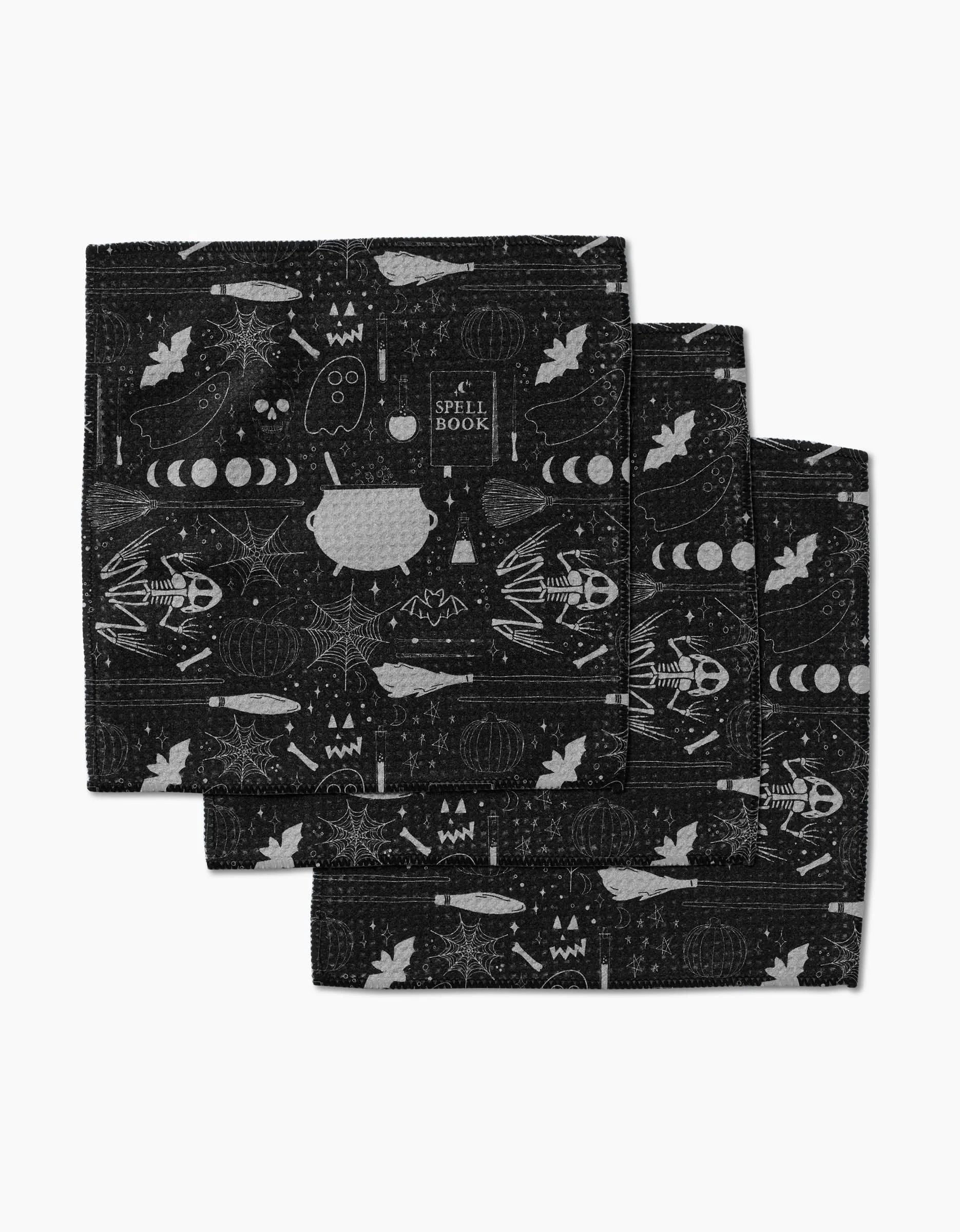 Rosa Kichline’s Witches Brew set includes three black cloth napkins made from super-absorbent Geoweave fabric, each featuring white Halloween-themed prints like skeletons, pumpkins, ghosts, bats, witch hats, and more.