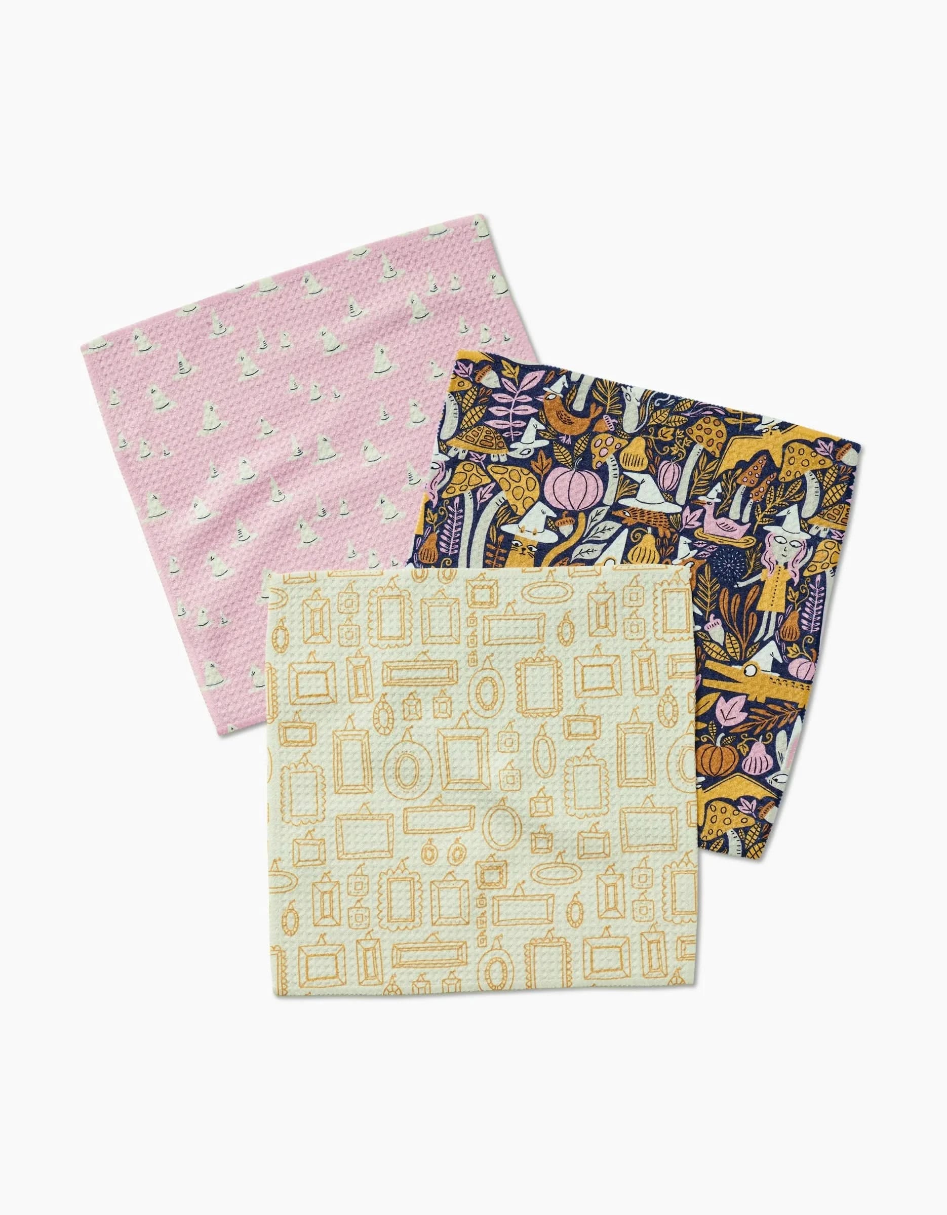 The Witchy Season napkins by Amy MacCready are a set of three reusable cloths: pink with white flowers, dark blue with botanical and animal prints, and cream with gold frames—all made from recycled materials.