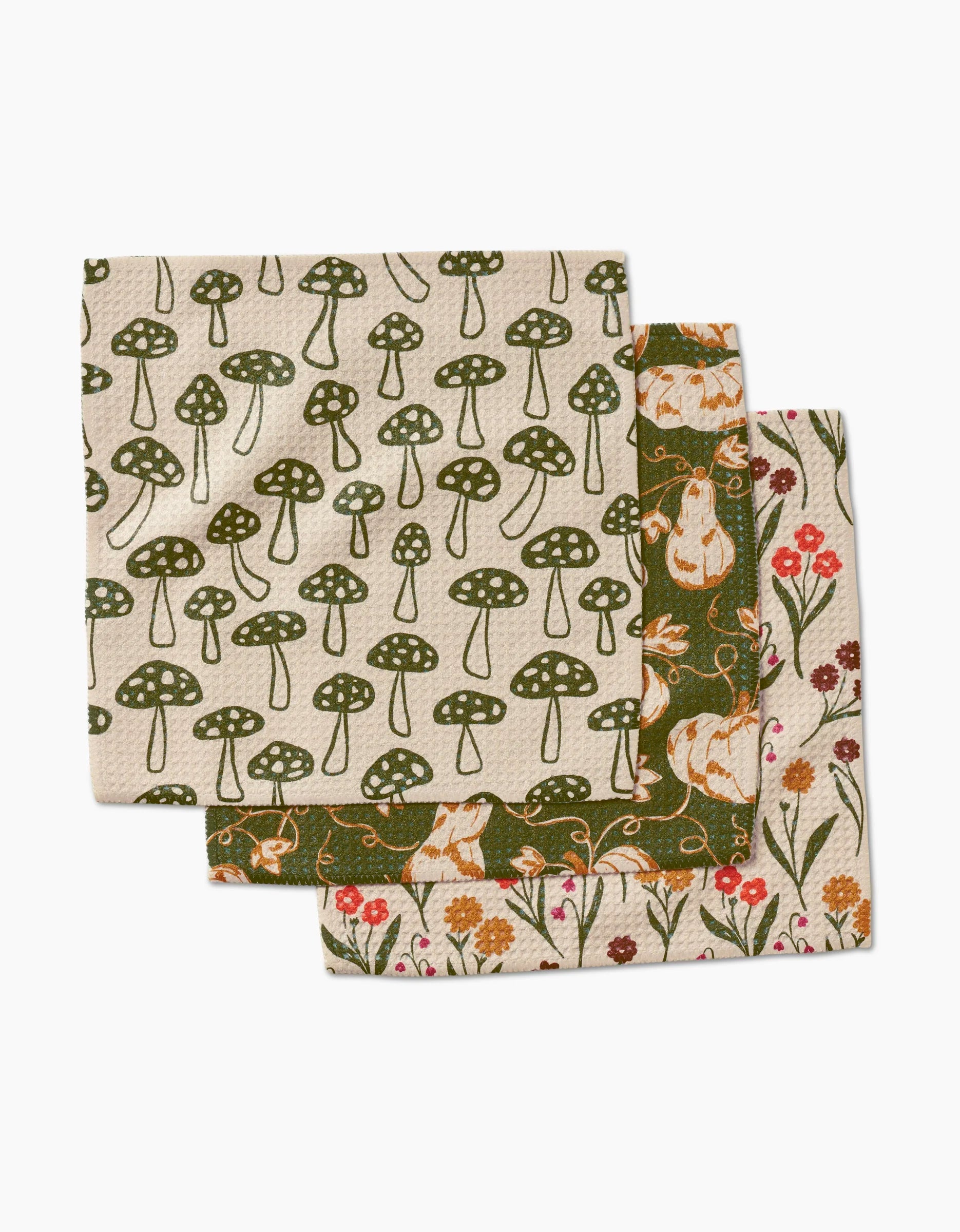 Three reusable cloths from Kayla Anns Woodland Trail set are stacked and slightly overlapping, featuring nature-themed, super-absorbent dishcloths with green mushrooms, white rabbits with pumpkins, and red and yellow flowers on beige backgrounds.