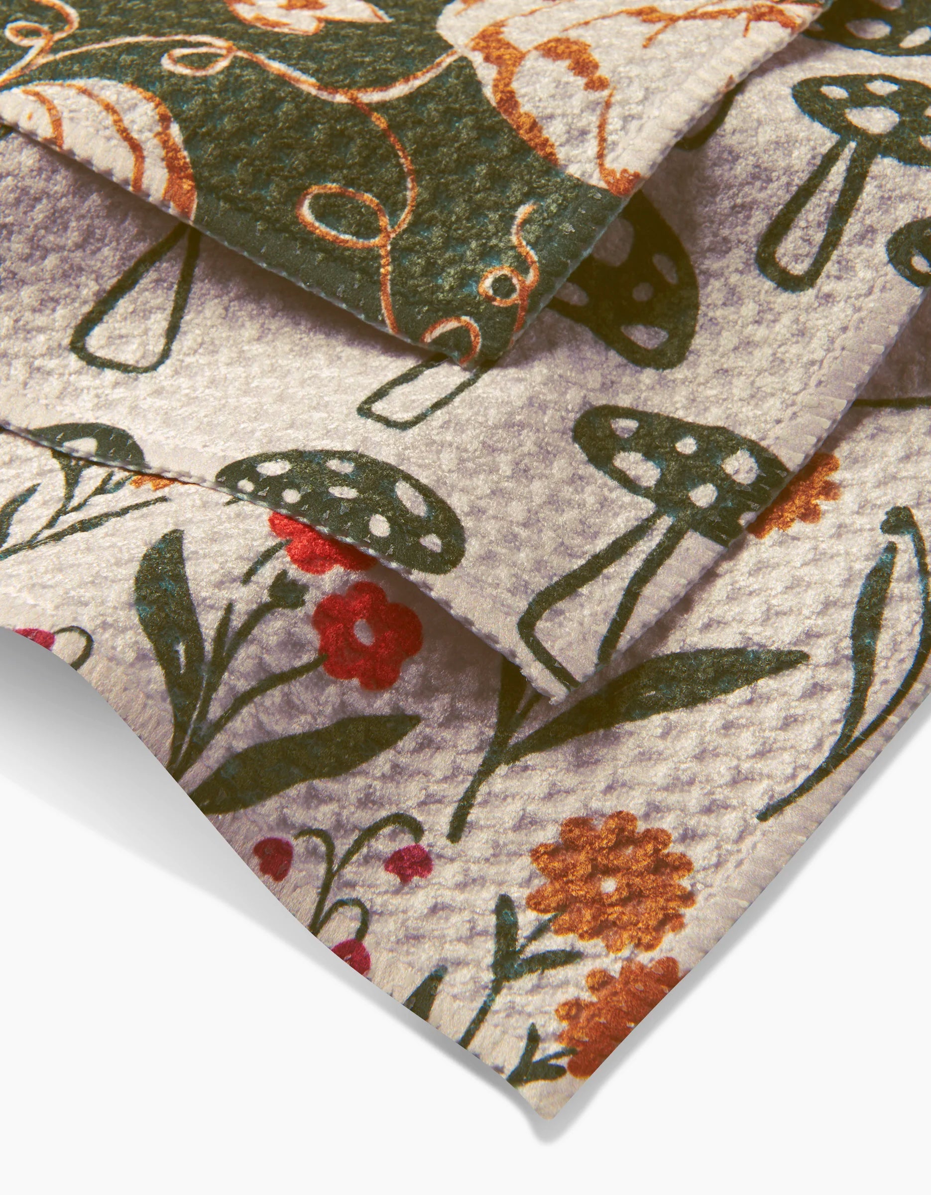Close-up of Kayla Anns Woodland Trail Geoweave dishcloth set, featuring whimsical green, red, and orange botanical and mushroom prints on cream—stylish and super-absorbent for any kitchen.