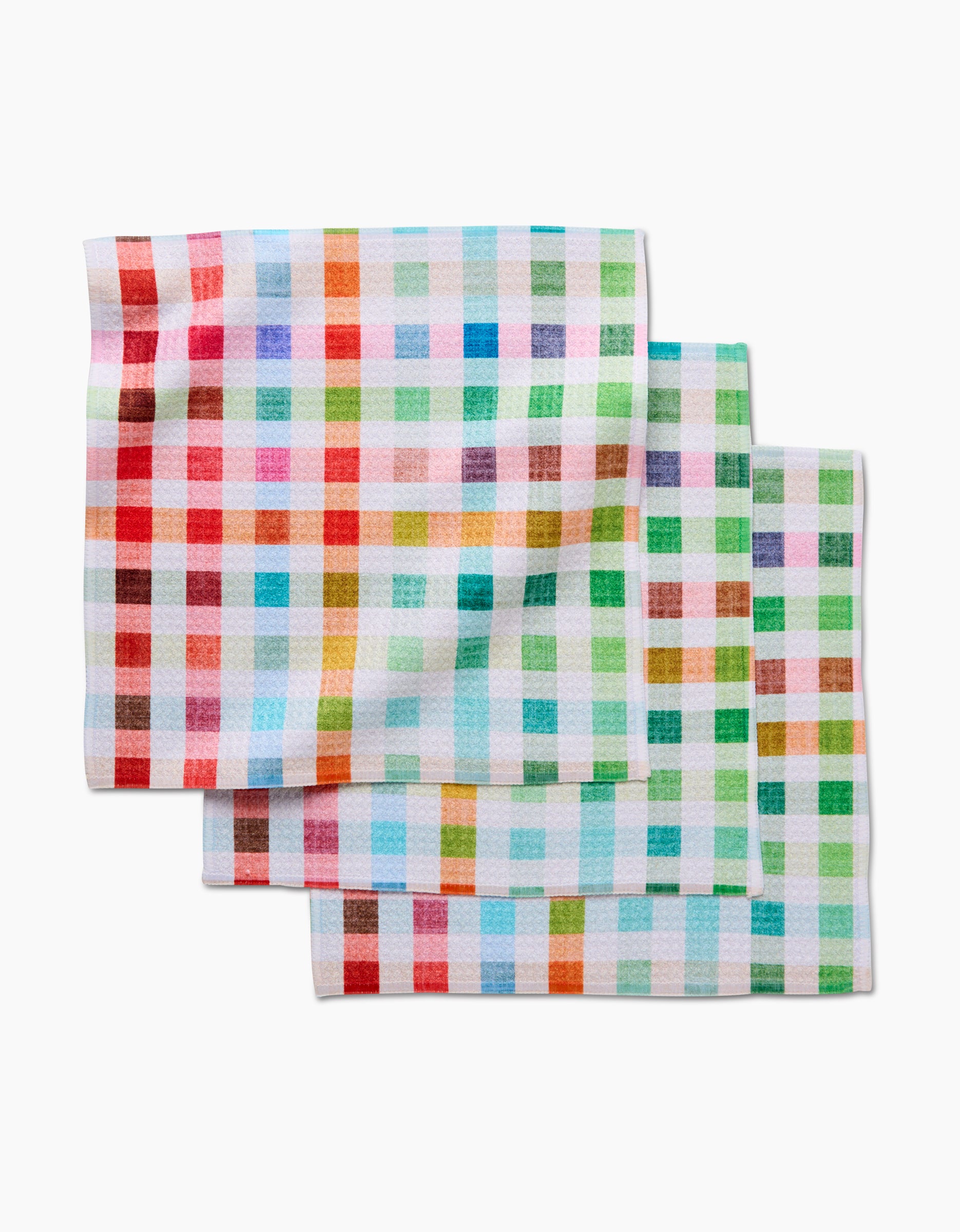 Three Woven Spring Plaid dish towels by Pascale Dilger are stacked, each made from soft Geoweave fabric with a vibrant plaid pattern in red, green, blue, and orange squares on a white background.