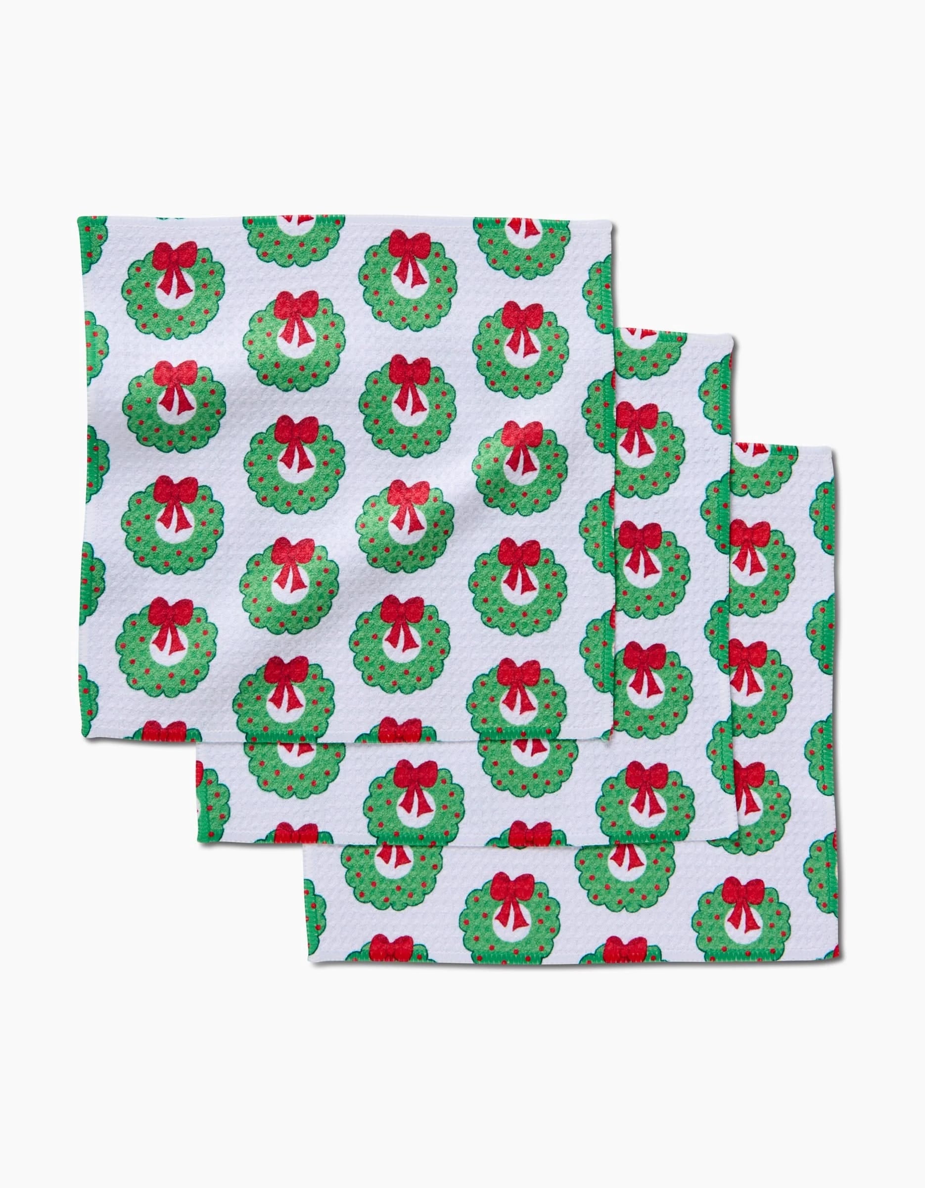 The Mindfulnice Wreath Wishes set includes three white Geoweave kitchen towels, each featuring green Christmas wreaths with red bows in an all-over festive pattern.
