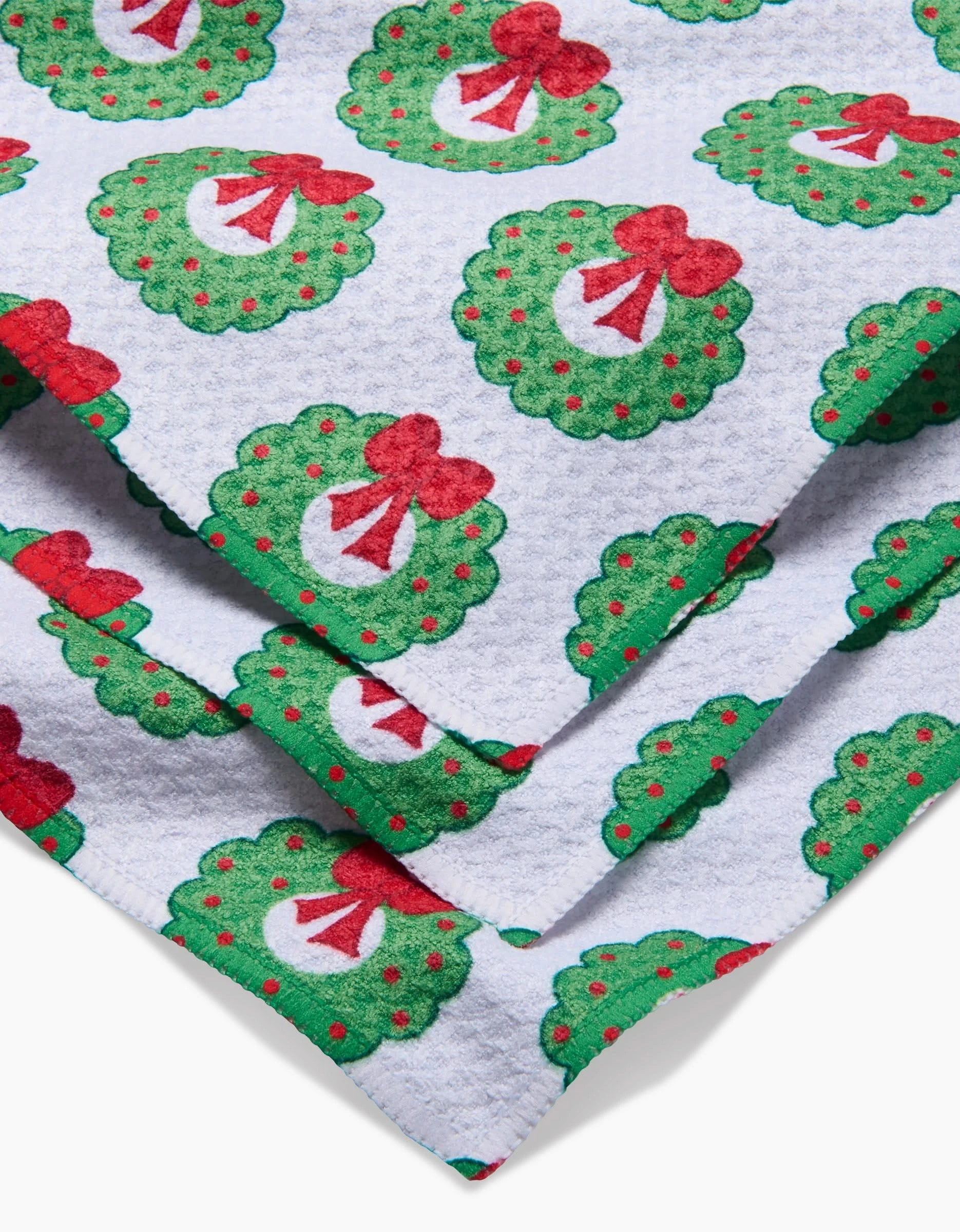 A close-up of Mindfulnice’s Wreath Wishes Geoweave fabric, showing festive green wreaths with red bows and dots—perfect for a holiday kitchen towel or dishcloth set.