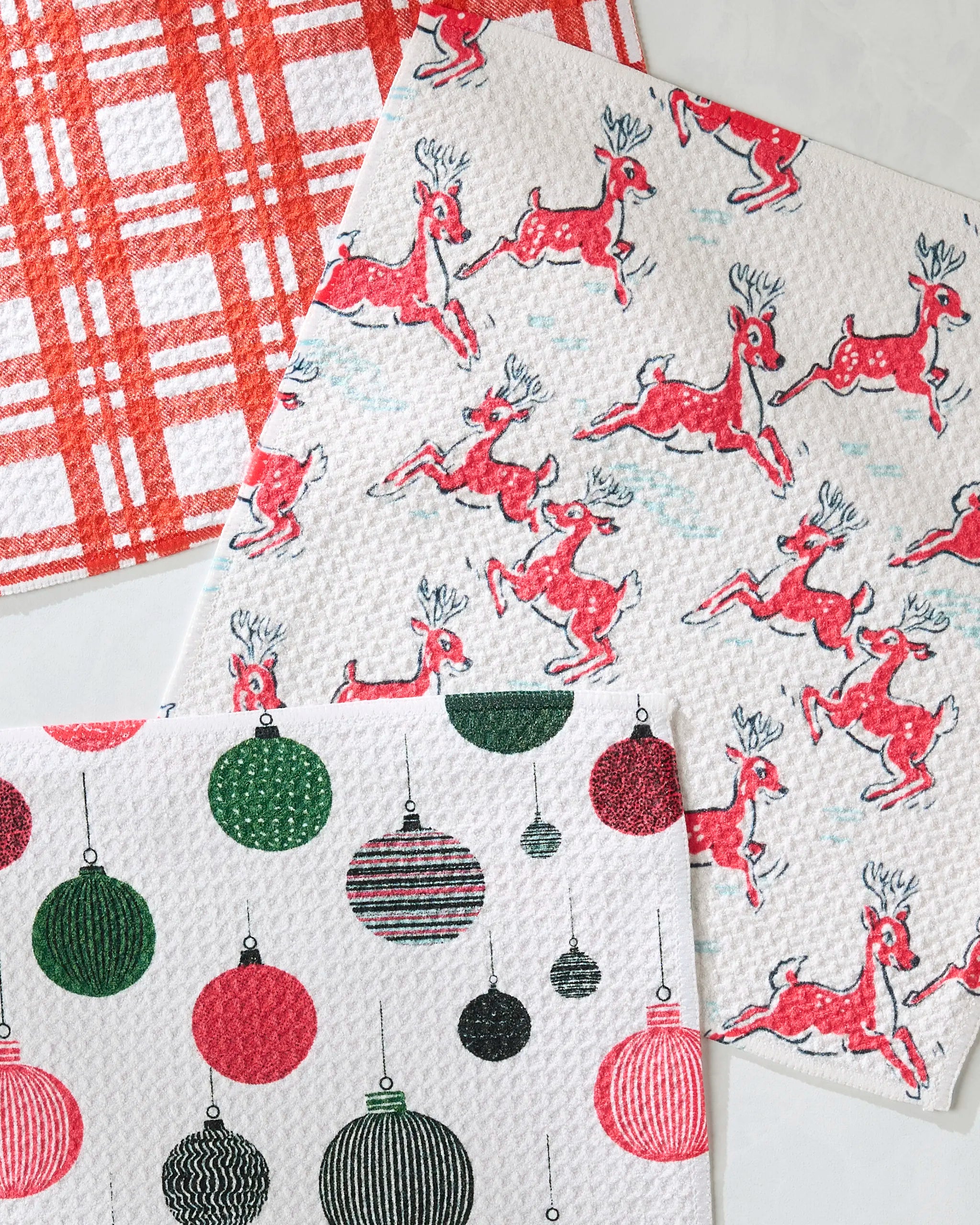 The Geometry Xmas Day dishcloth set includes three super-absorbent dishtowels in red plaid, red reindeer, and green and red Christmas ornament designs—perfect for adding festive cheer to your holiday kitchen.