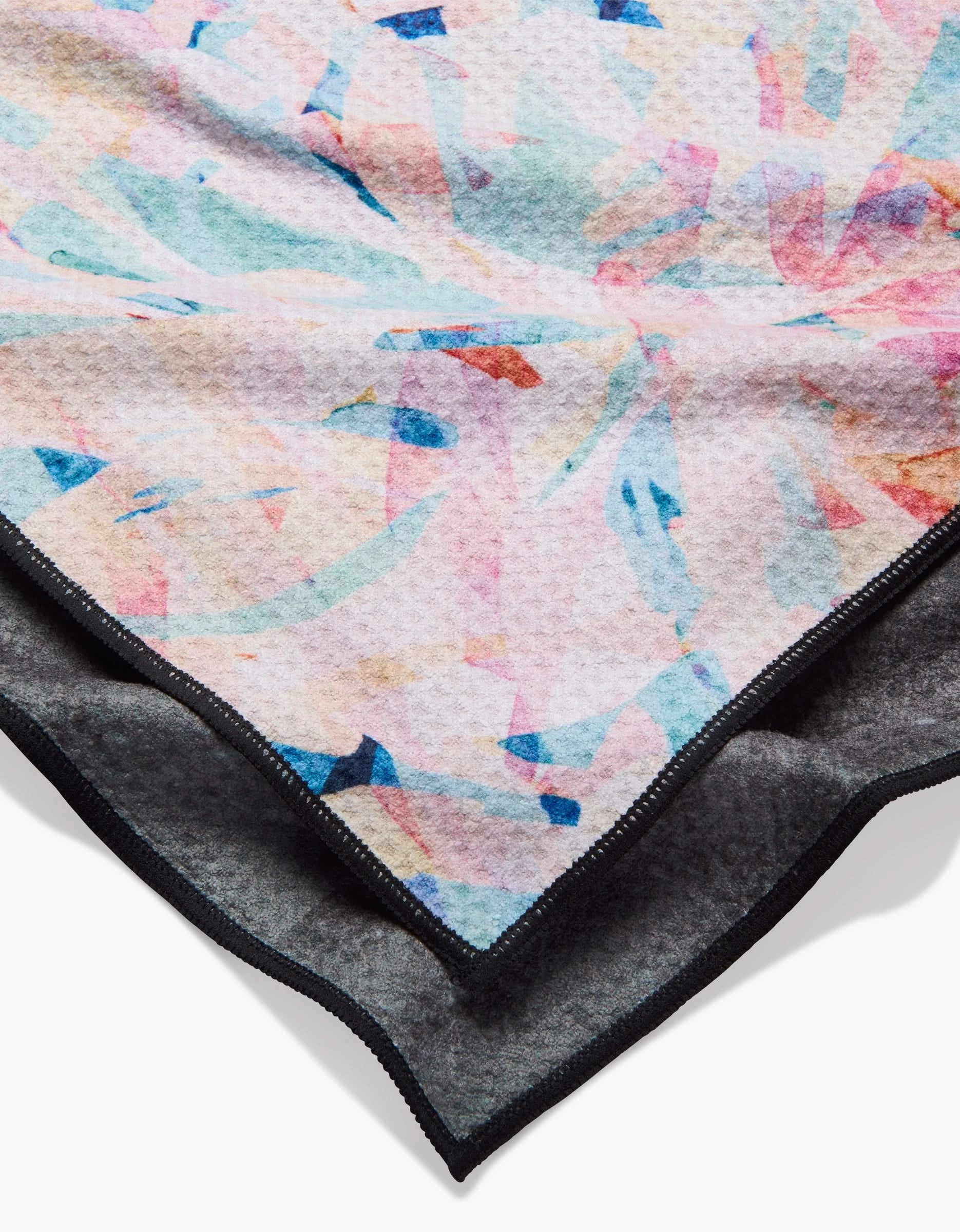 A close-up of Rachel Parkers Abstract Jungle Dog Towel shows its soft, absorbent fabric with a vibrant pink, blue, and light pattern on one side and solid dark gray on the other—finished with black edges for quick drying.